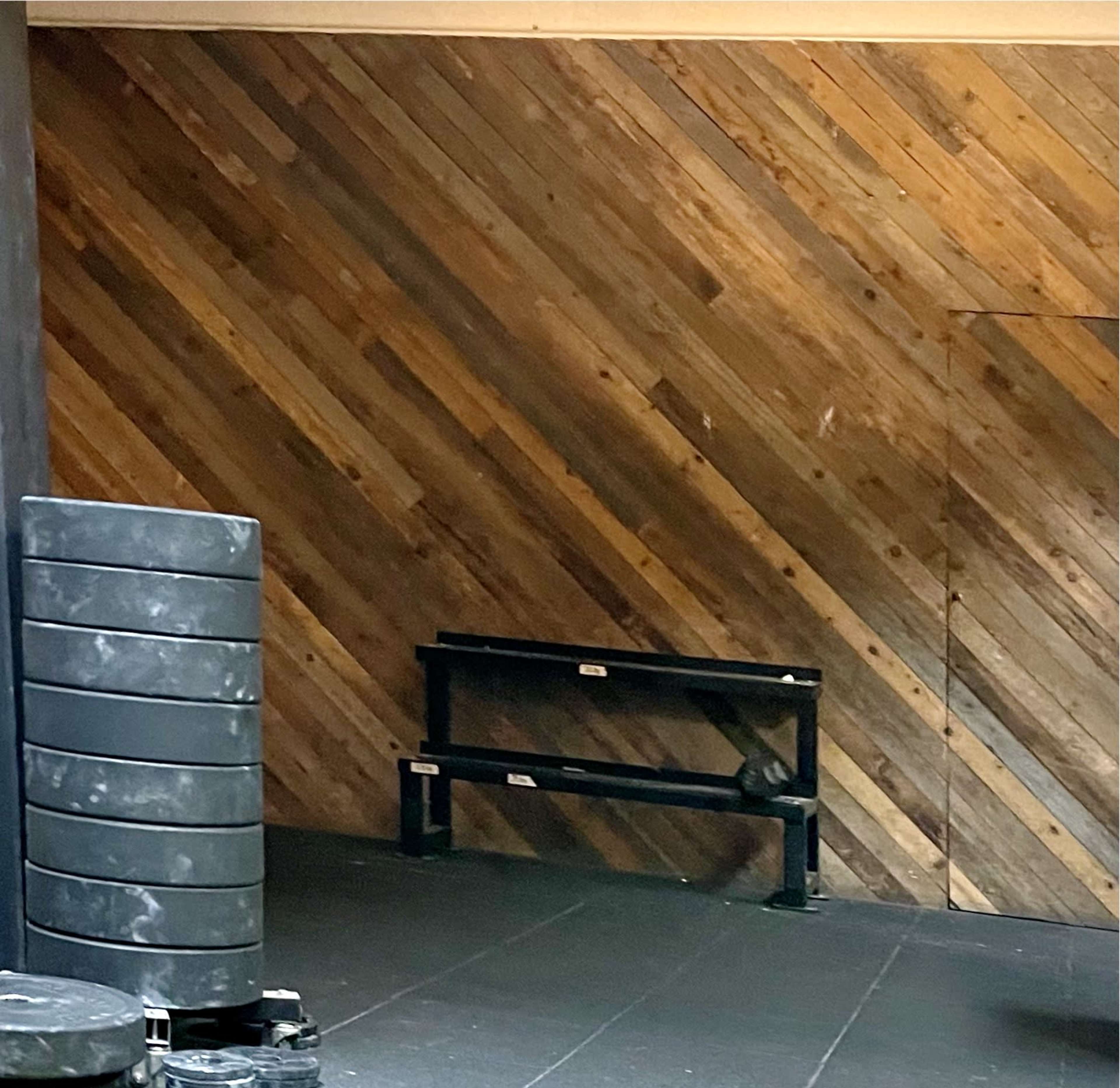 A gym setting with a stacked weight plate on the left and a black bench positioned against a wooden diagonal-paneled wall.