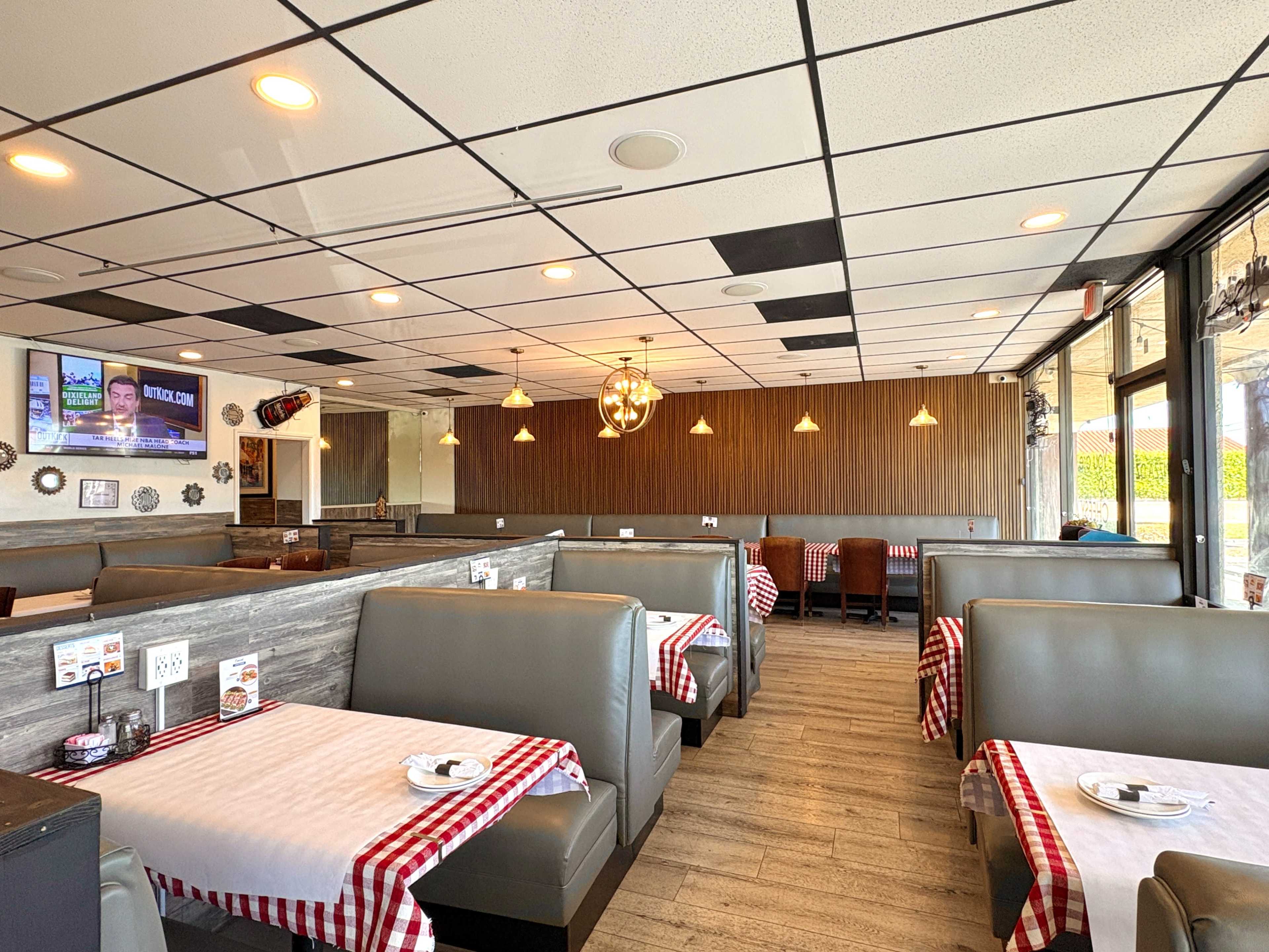 The image shows an empty restaurant interior with booth seating, red-checked tablecloths, and pendant lighting.
