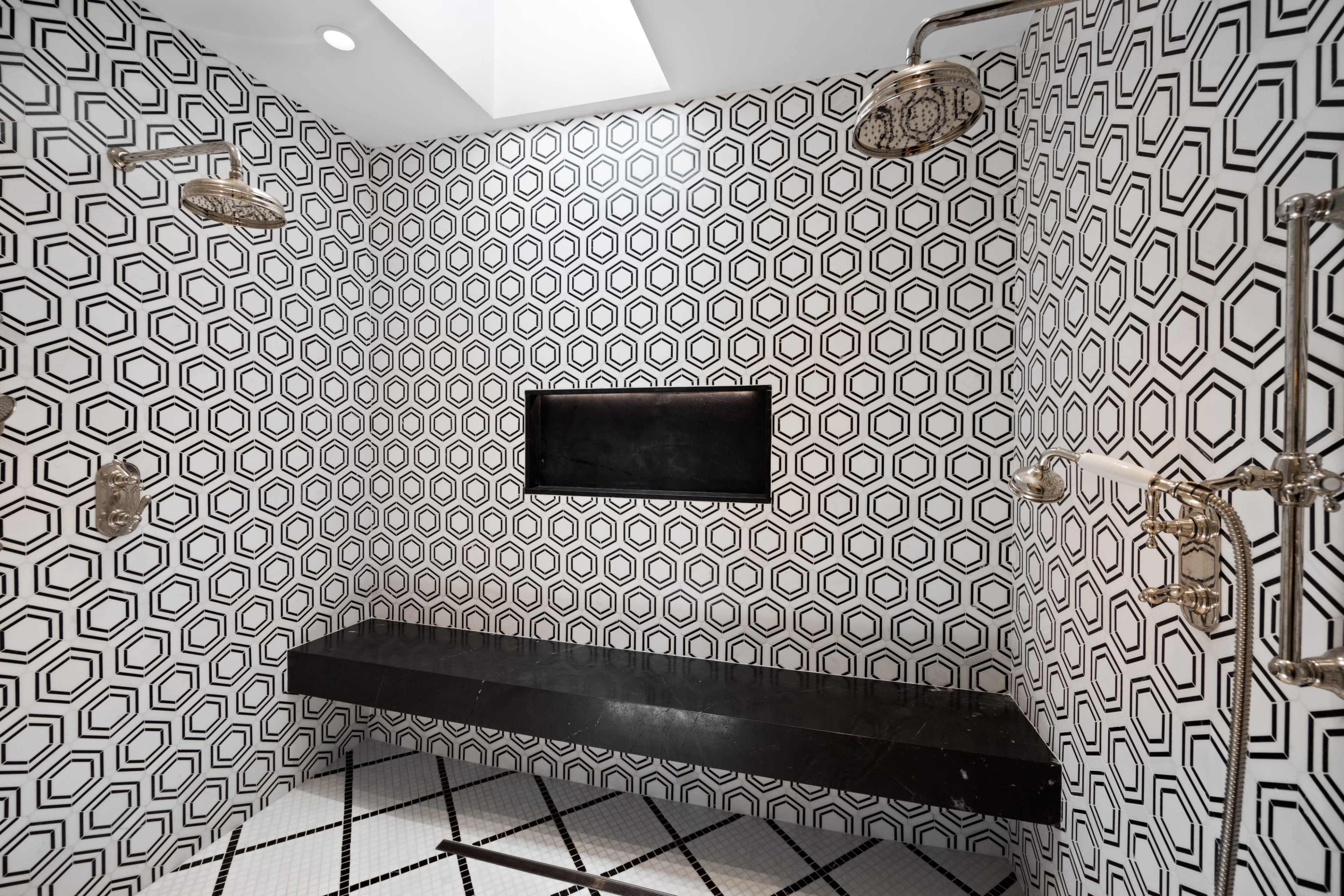 The image shows a modern shower area with hexagonal black and white tiled walls and a black stone bench.