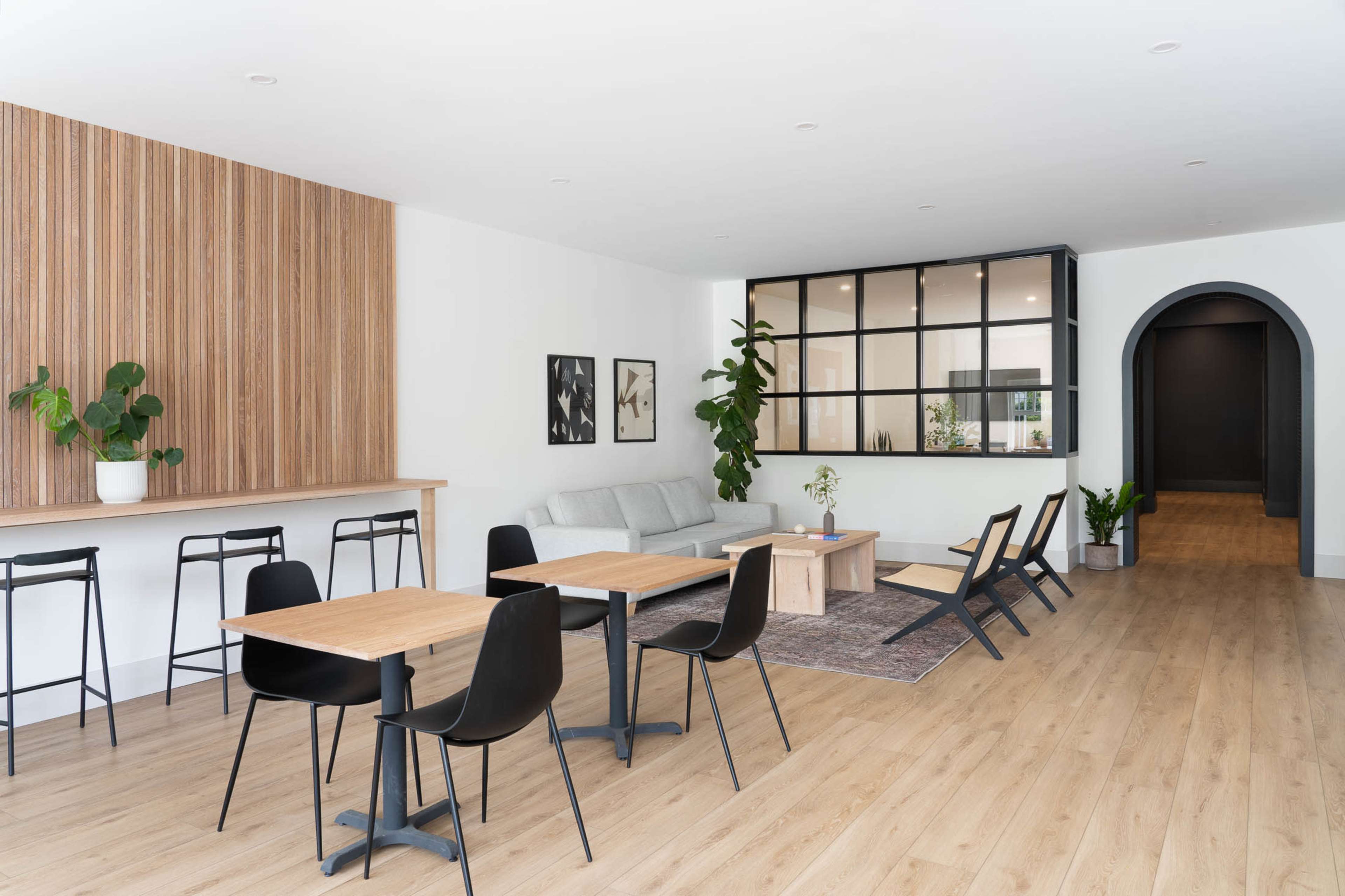 A modern interior space featuring a seating area with a sofa, wooden tables, and a glass-paneled partition.