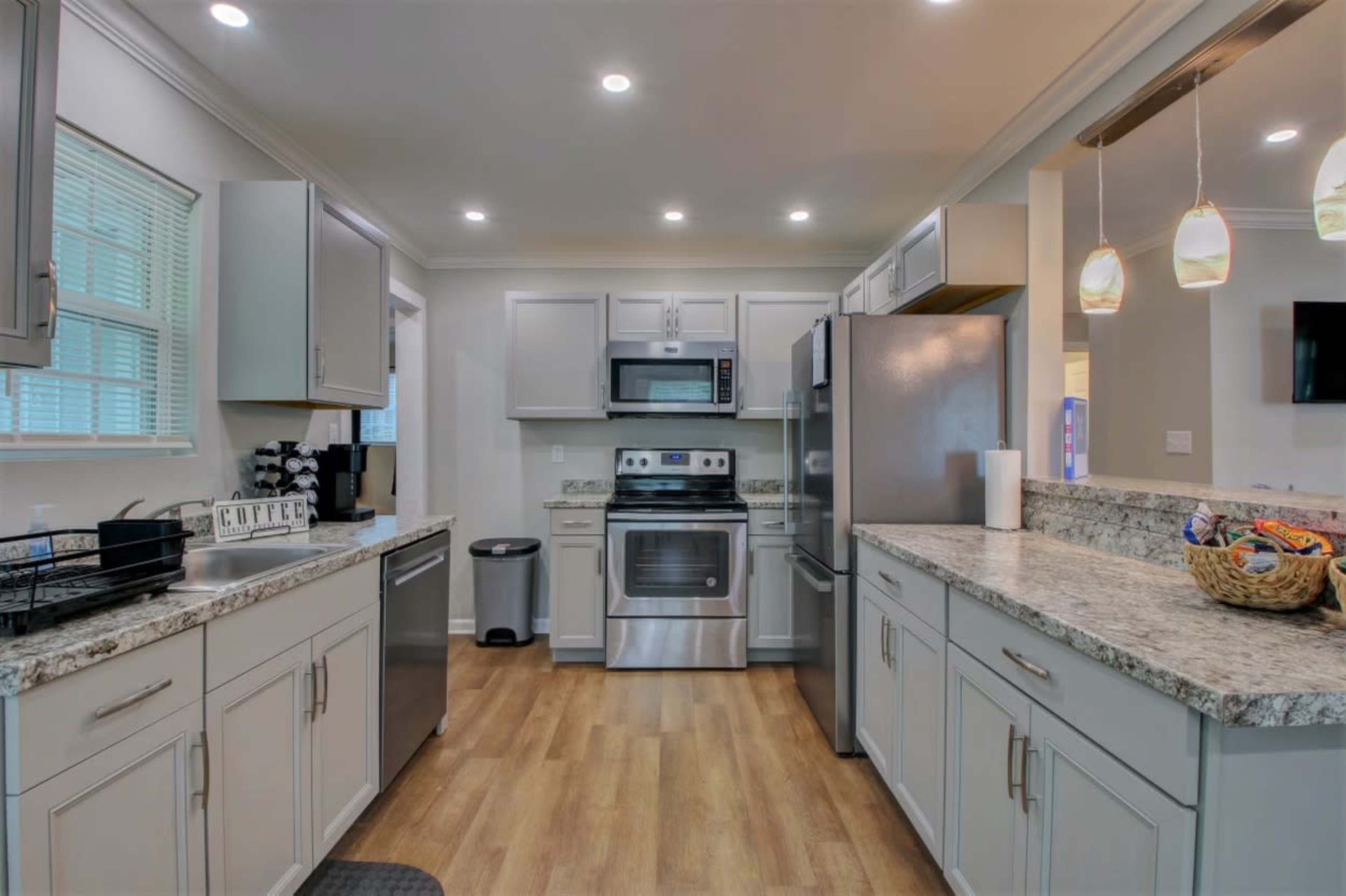 The kitchen features light gray cabinetry, stainless steel appliances, and a granite countertop with wooden flooring.