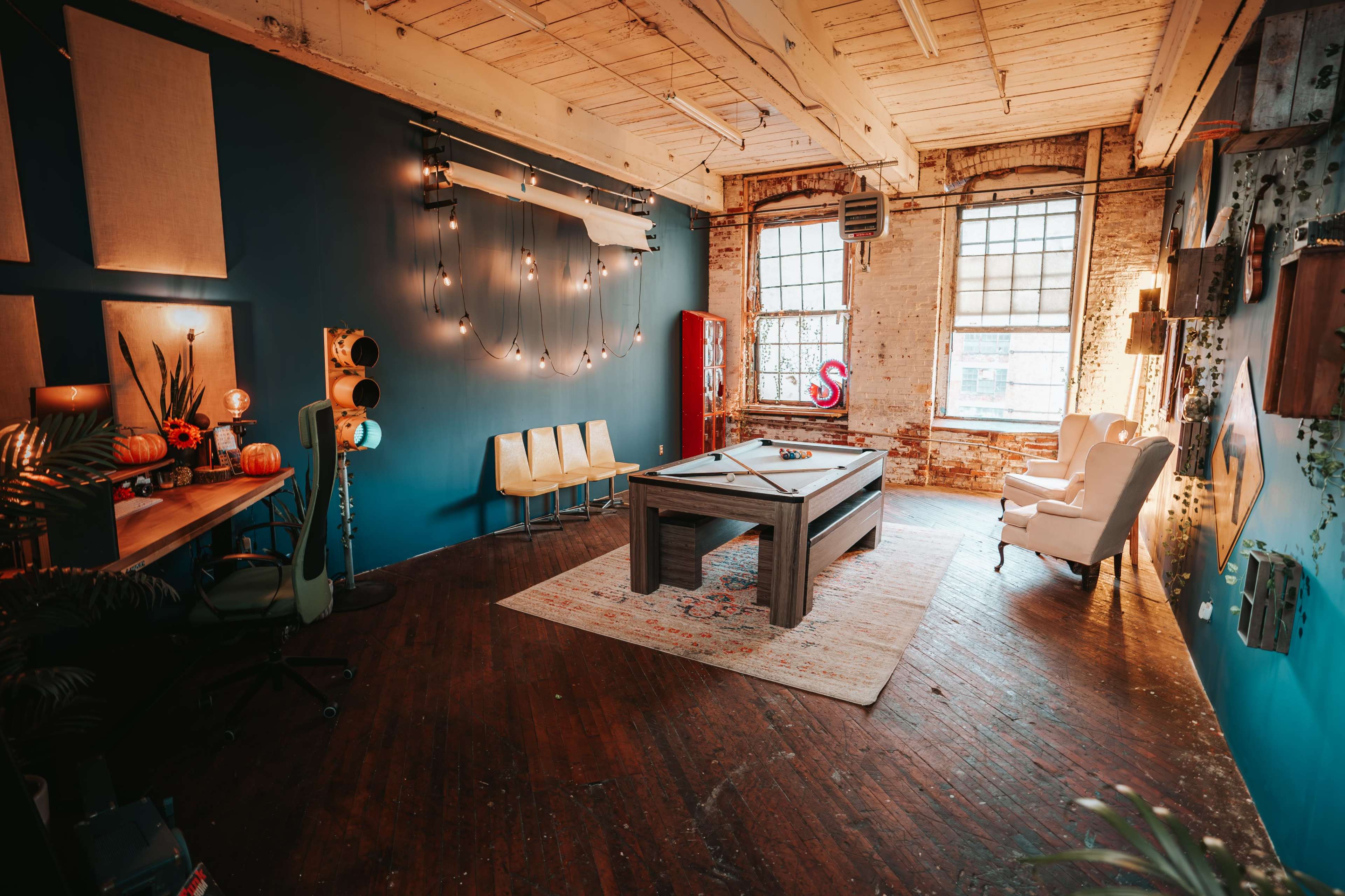 A spacious, well-lit room featuring a pool table at the center, surrounded by colorful decor and furniture.