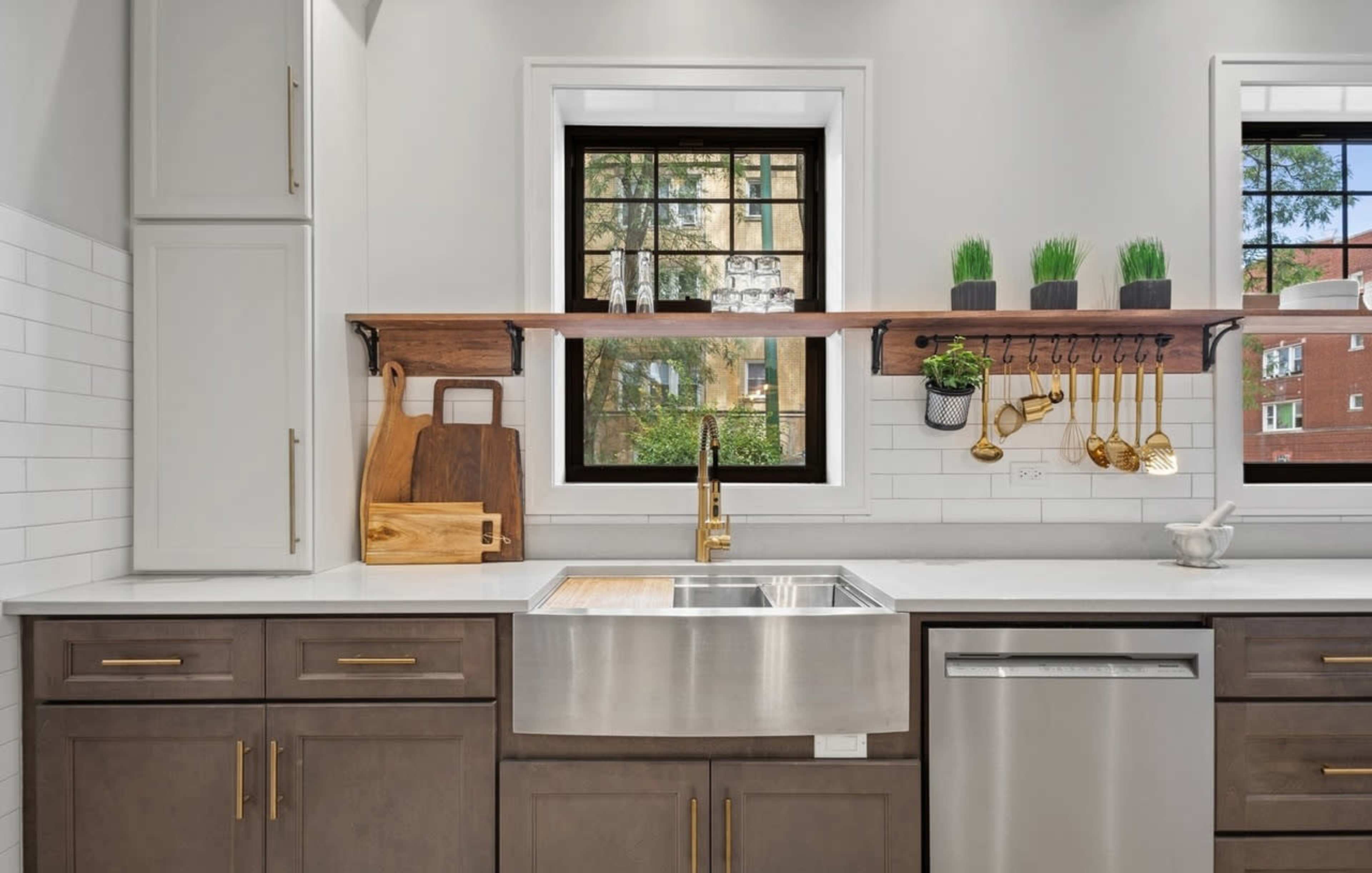 The kitchen features a farmhouse sink, a wooden countertop, and a mix of modern cabinetry with open shelving displaying kitchen tools and potted plants.