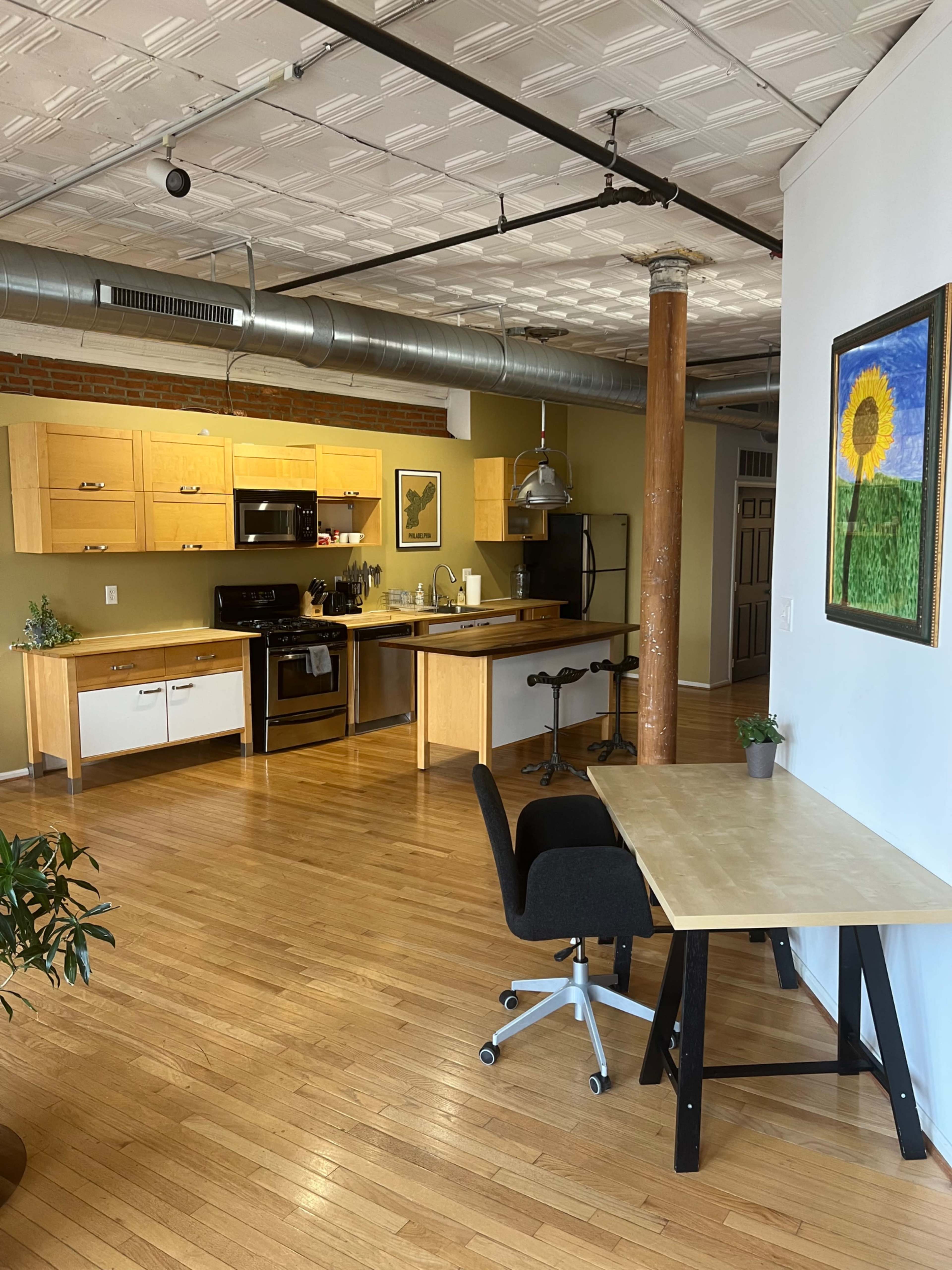 A modern open-concept kitchen and dining area featuring wooden cabinetry, a stainless steel stove, a central island, and a workspace with a desk and chair.