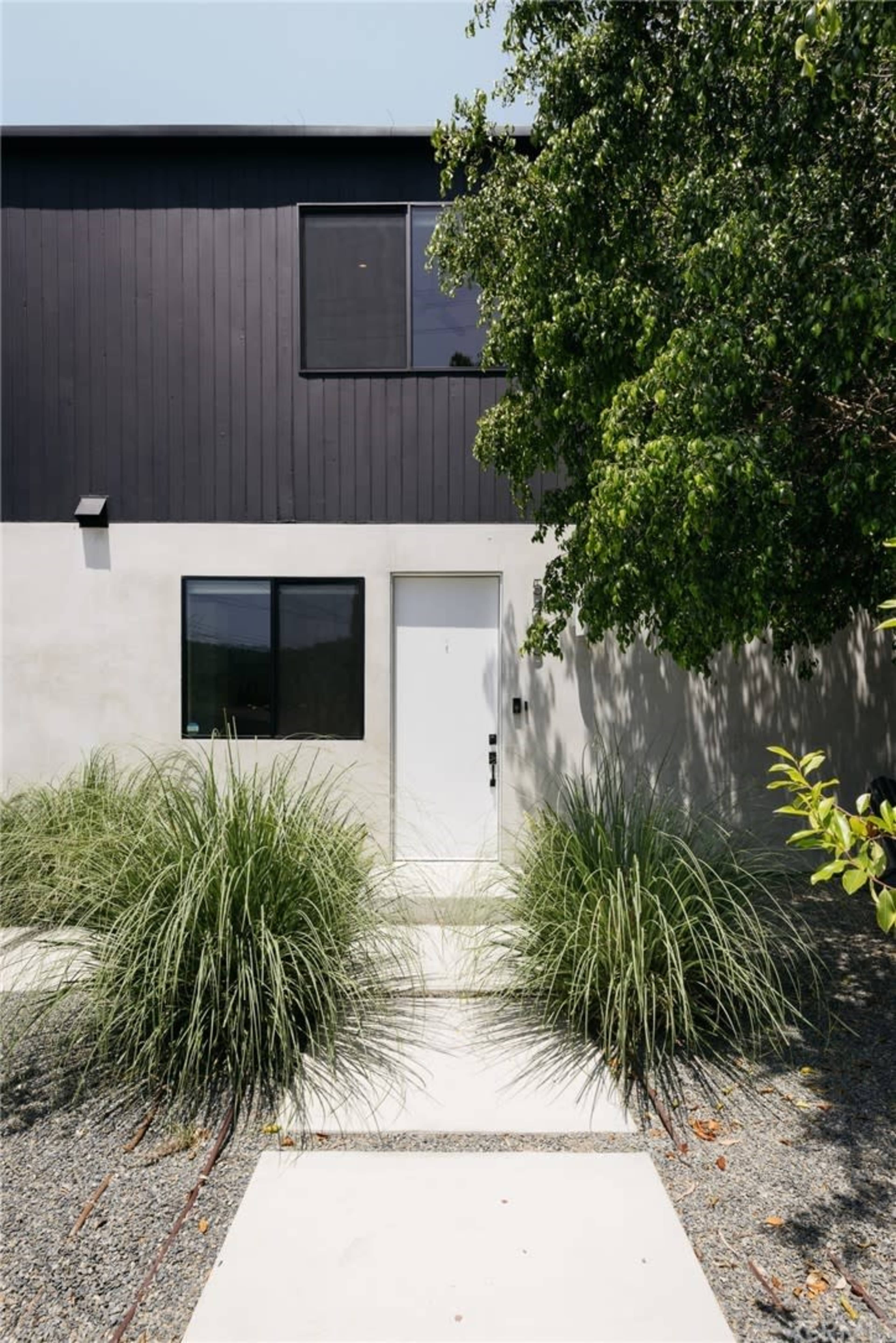 A modern home with a black upper section, white lower section, and a pathway lined with tall grass leading to the front door.
