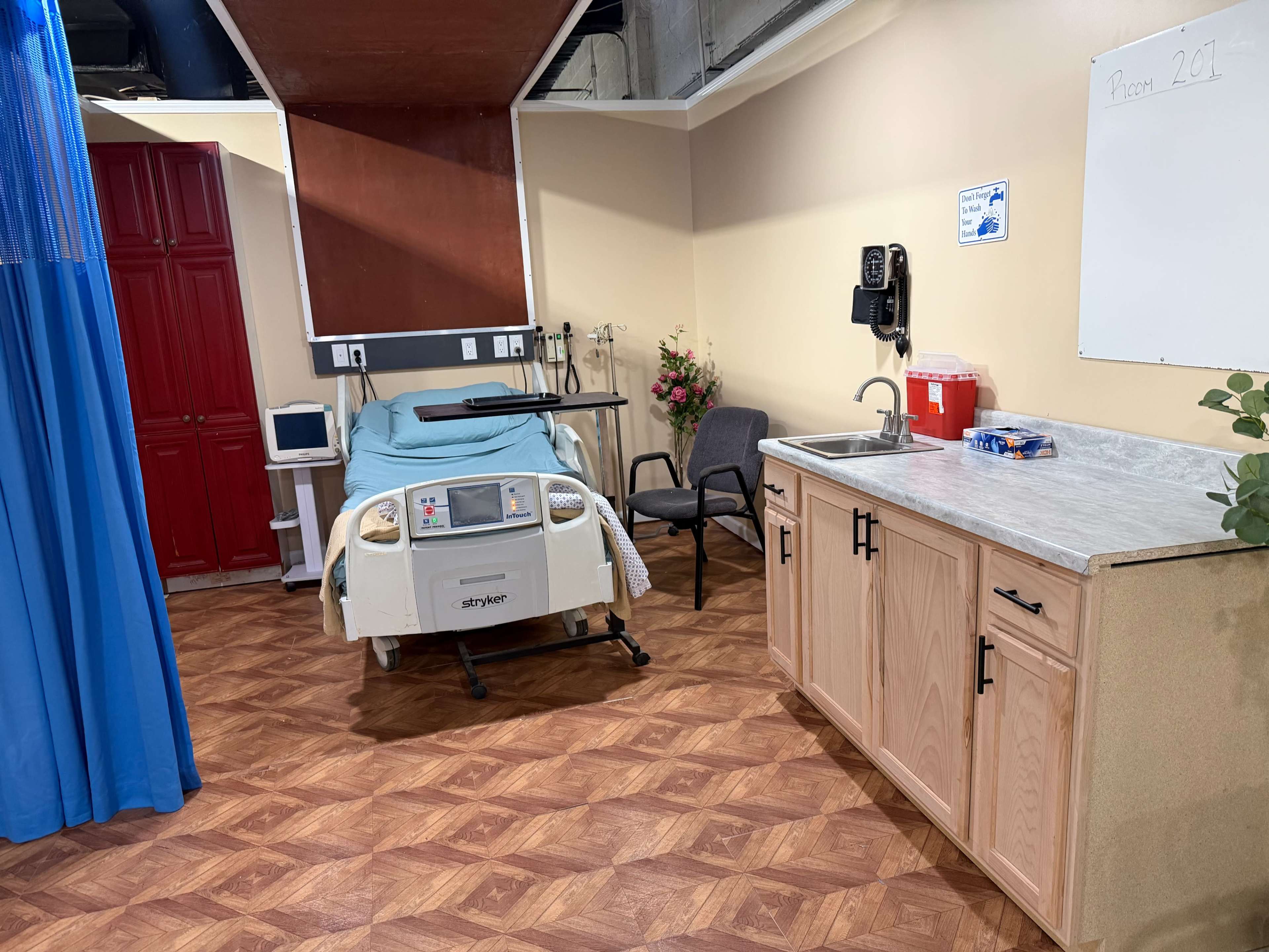 The image shows a hospital room featuring a bed, a chair, a cabinet with a countertop, and a whiteboard on the wall.