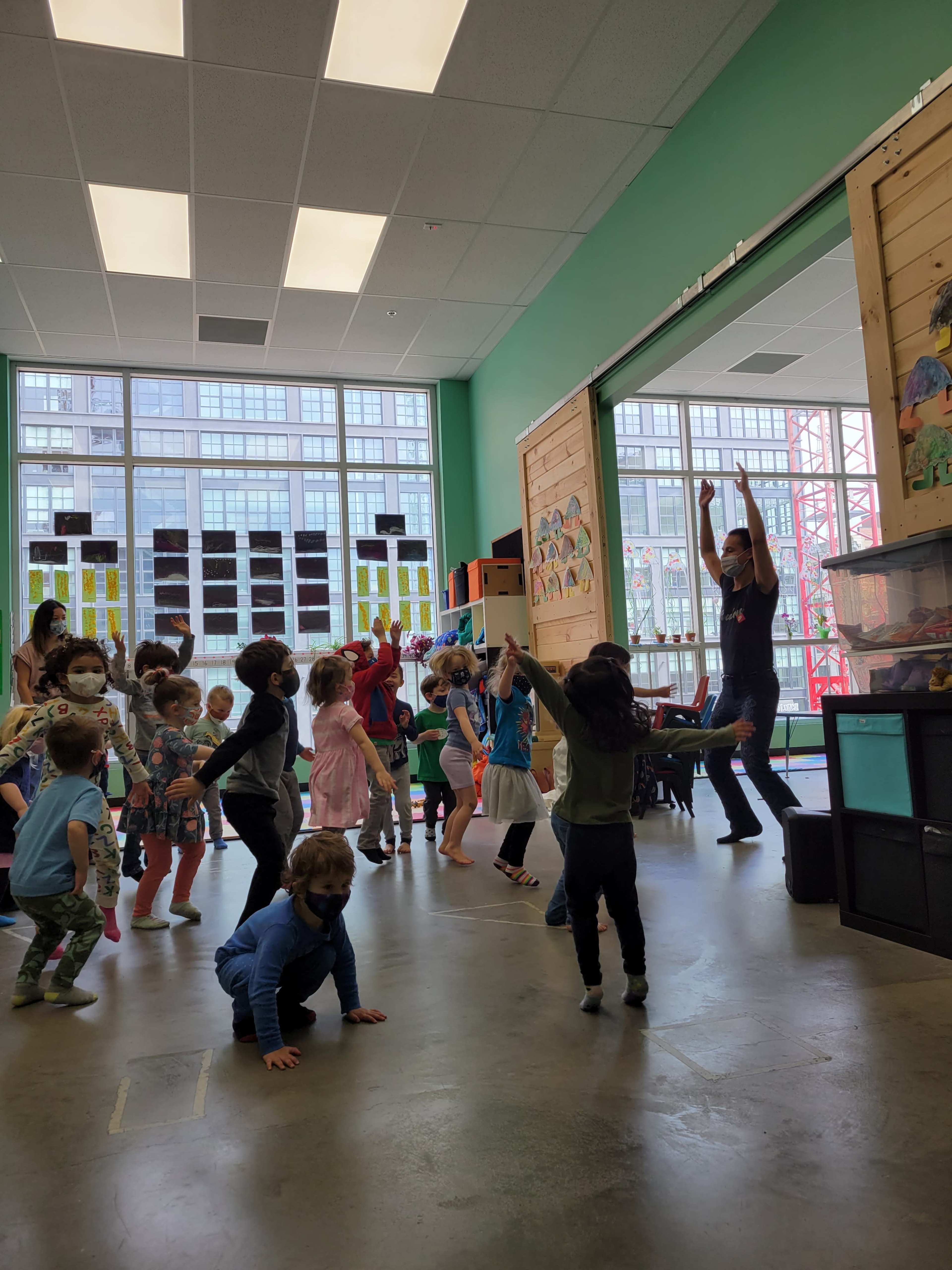 A group of children are engaged in a dance activity with an instructor in a brightly lit classroom.