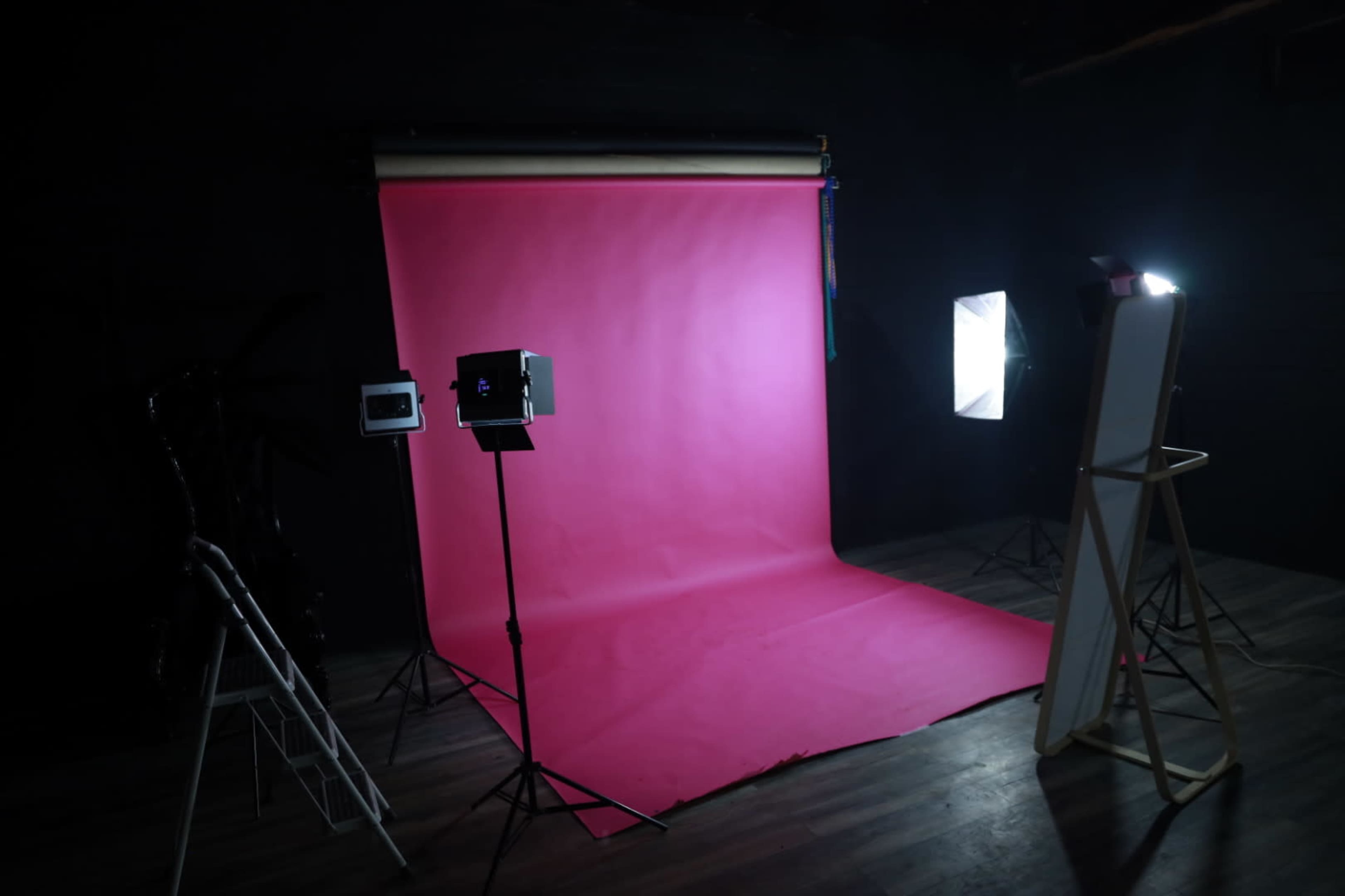 A photography studio setup with a pink backdrop, lighting equipment, and a standing mirror.