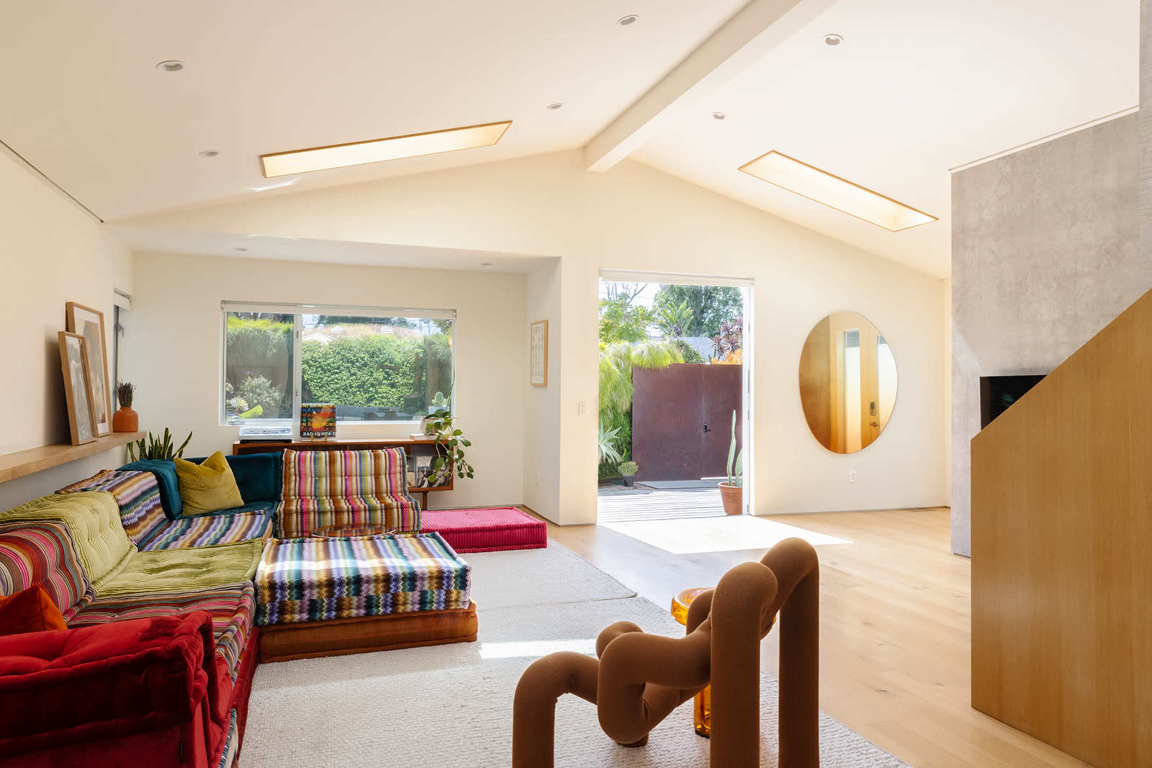 A modern living room with a colorful sectional sofa, large windows, and an open layout that connects to an outdoor space.