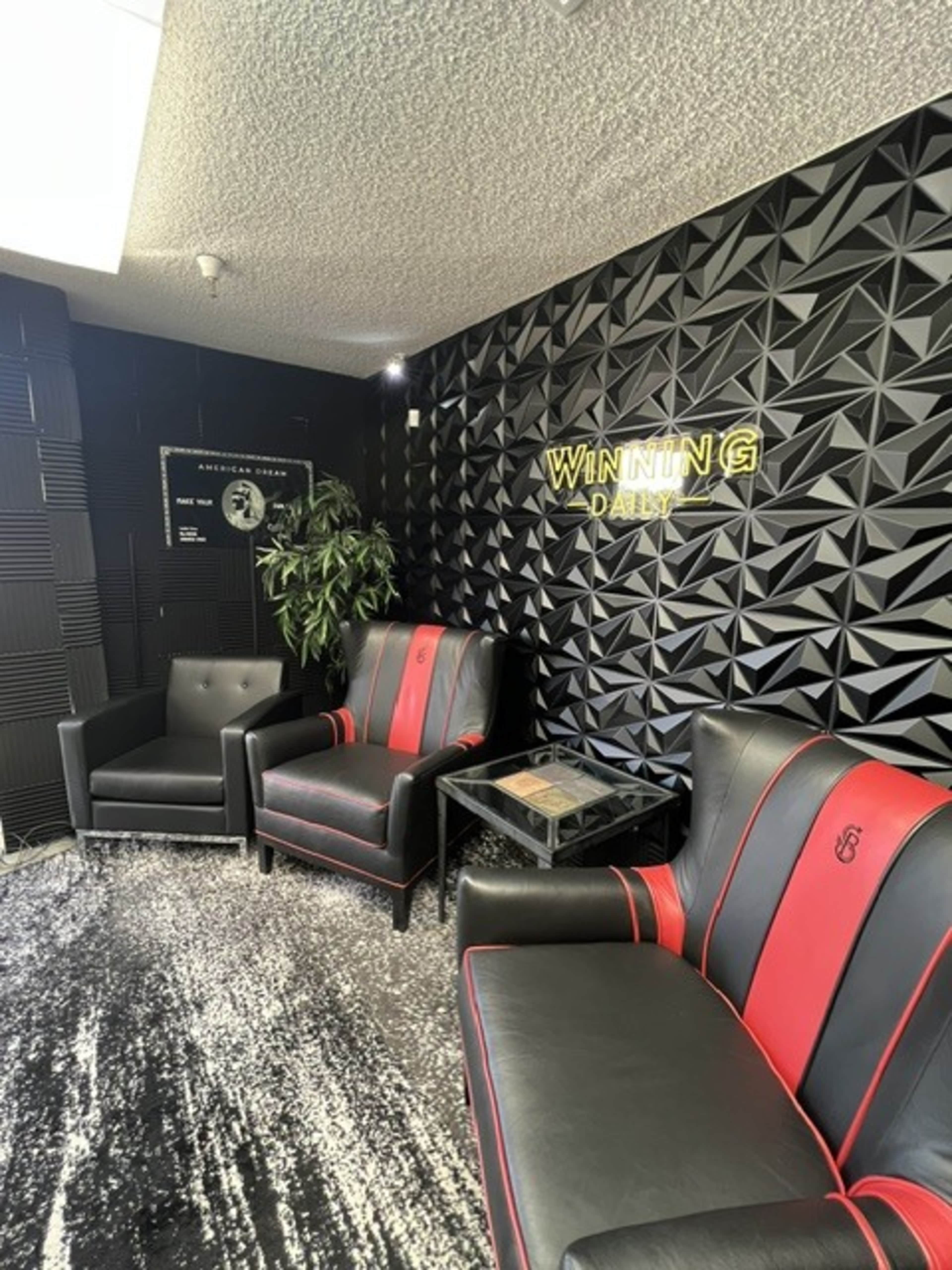 The image shows a modern waiting area featuring black and red leather chairs, a small black table, a decorative plant, and a textured black wall with the words "WINNING DAILY" in bright lettering.