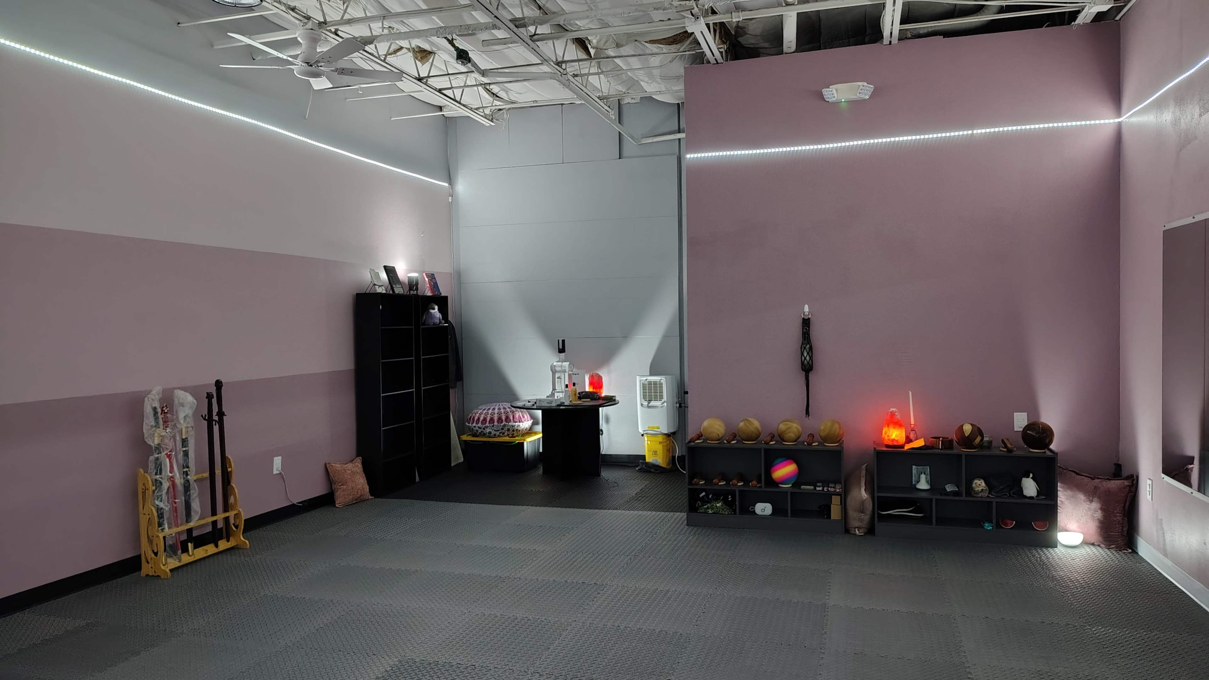 A spacious room with pink walls features a black shelf unit, various decorative items, and soft lighting along the ceiling.