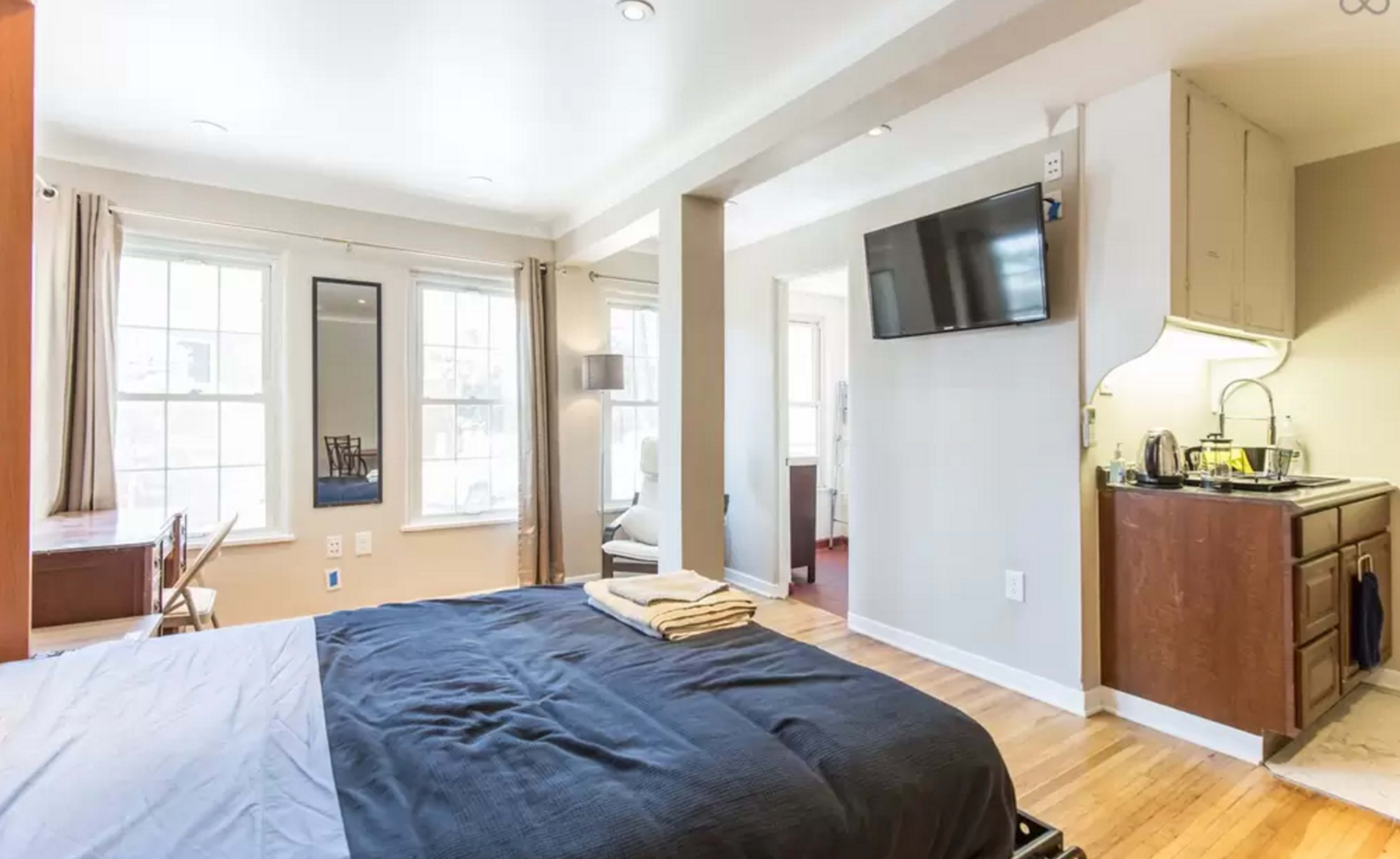 A bedroom with a bed, a television mounted on the wall, and a small kitchenette area.