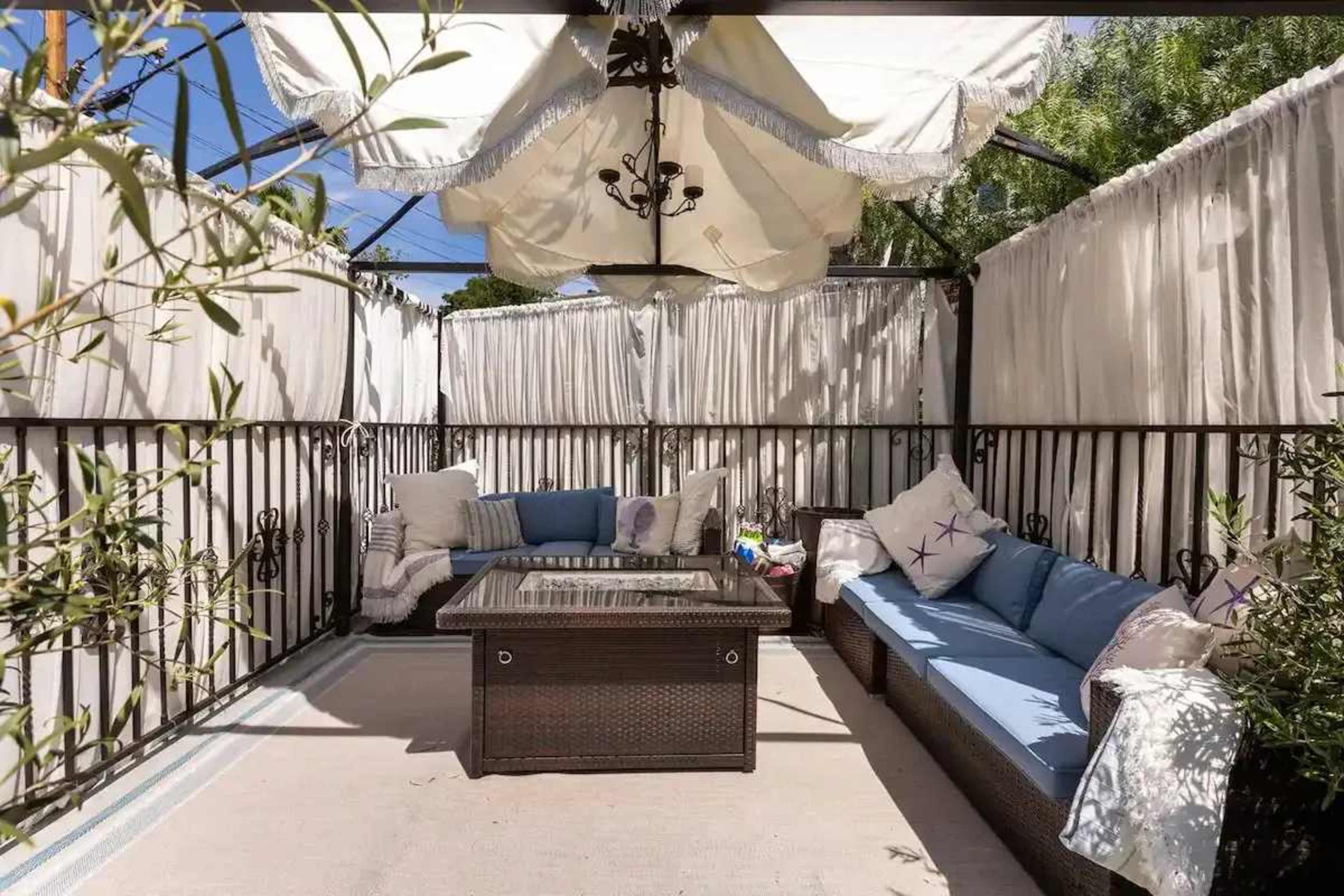 The image shows a patio area with a covered seating arrangement featuring a table and a sofa, surrounded by fabric drapes for privacy.