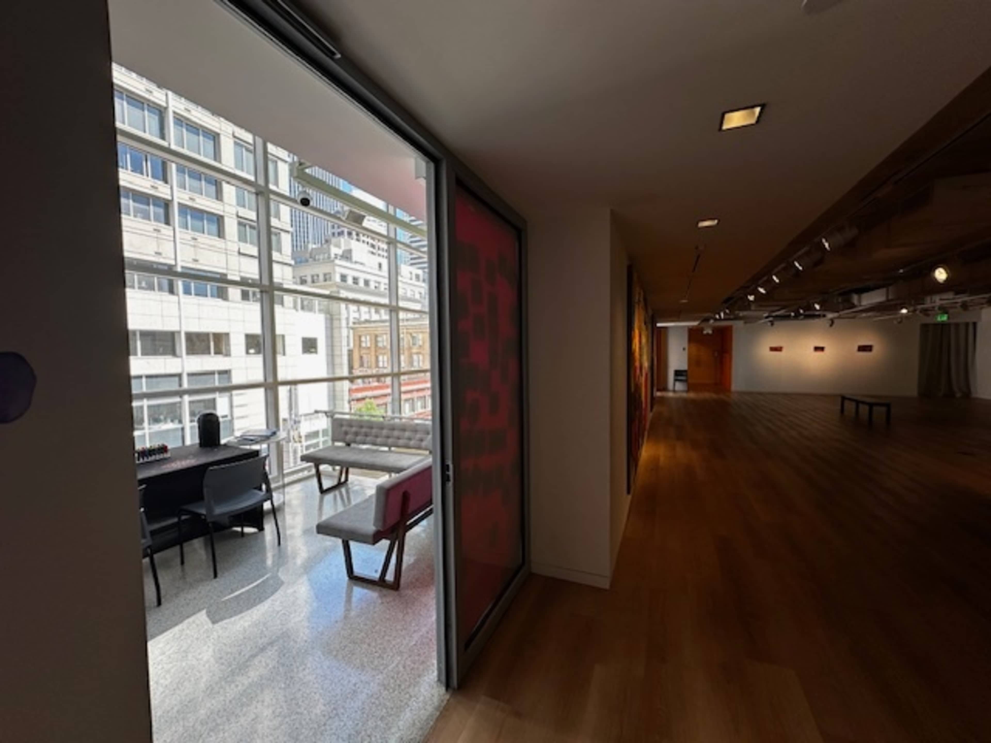 A modern indoor space with large windows, featuring a seating area adjacent to an art-lined hallway.