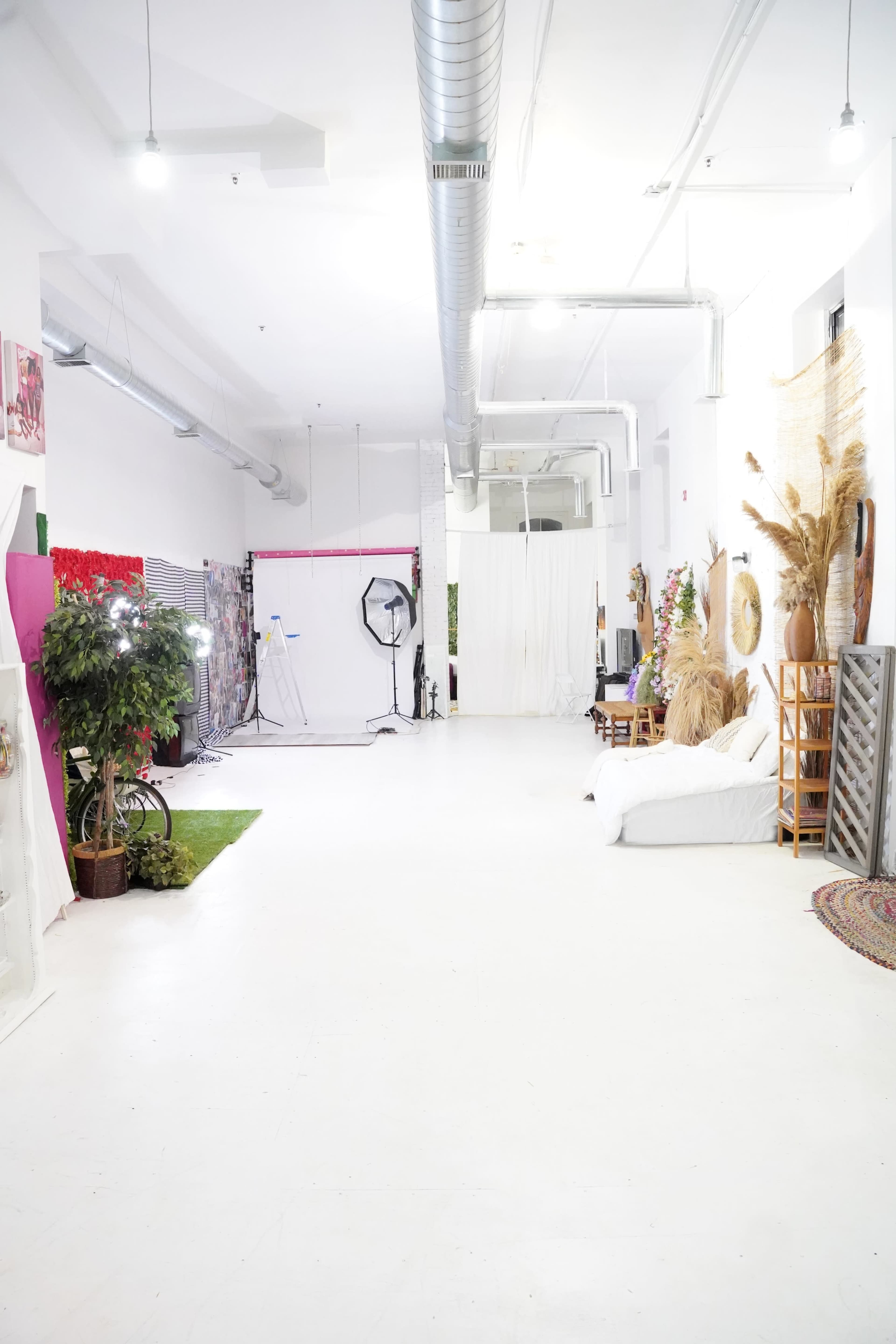 A spacious studio with a white floor, various photo backdrops, and decorative elements like plants and textiles.