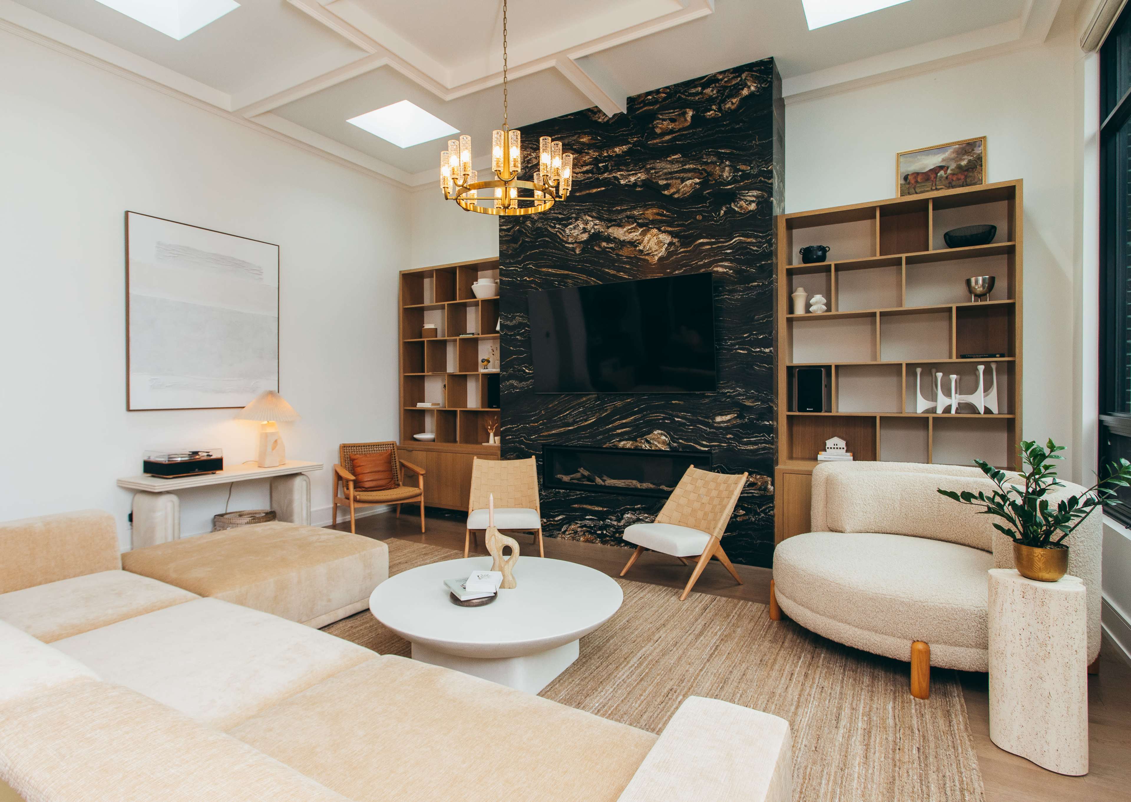 A modern living room features a plush sectional sofa, a round coffee table, and a large wall-mounted television against a striking dark stone accent wall.