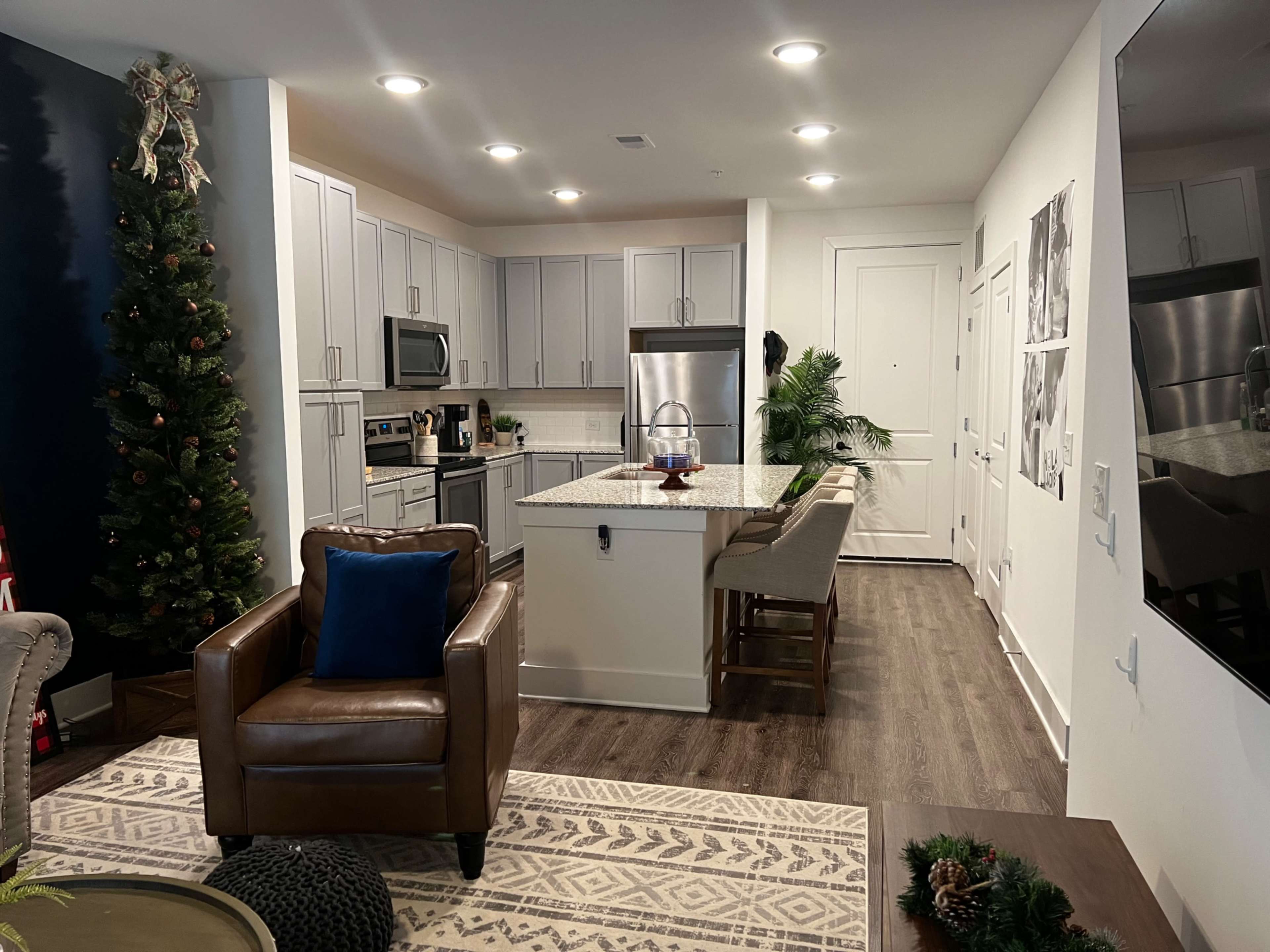 A modern kitchen and living area with white cabinets, stainless steel appliances, and a Christmas tree in the corner.