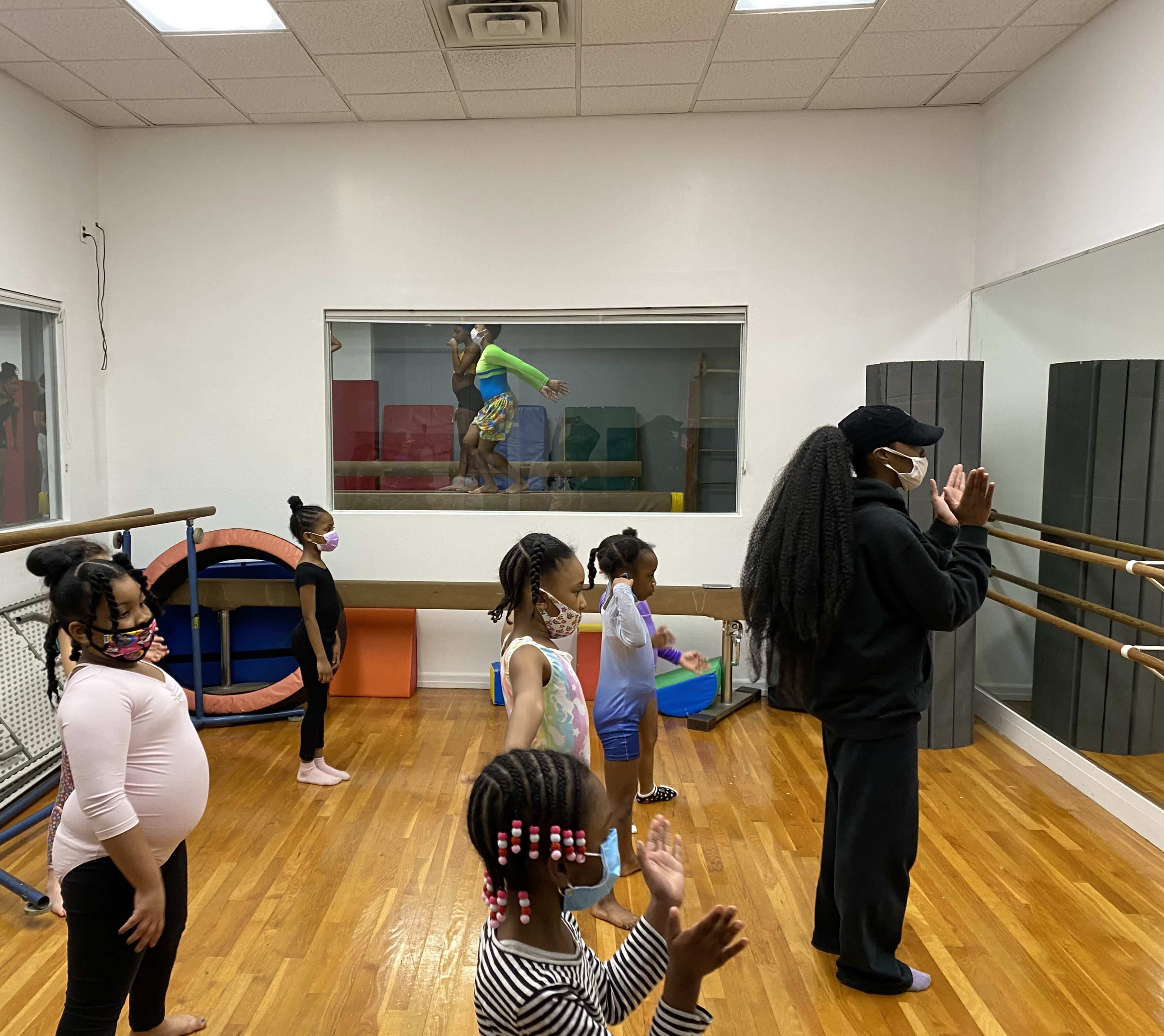 A group of children in dance attire are practicing their moves in a dance studio with a mirrored wall.