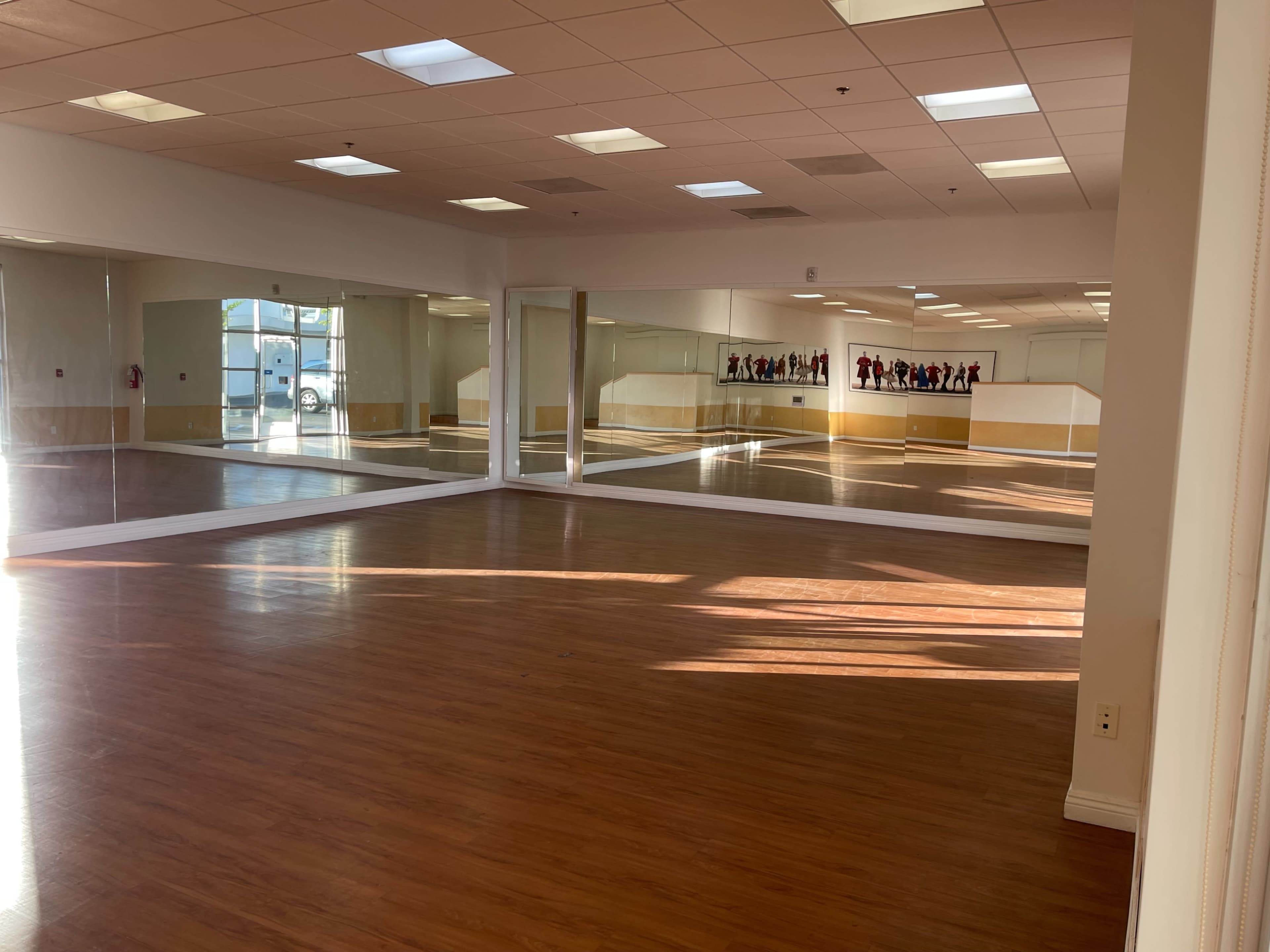The image shows an empty dance studio with wooden flooring and large mirrors on the walls.