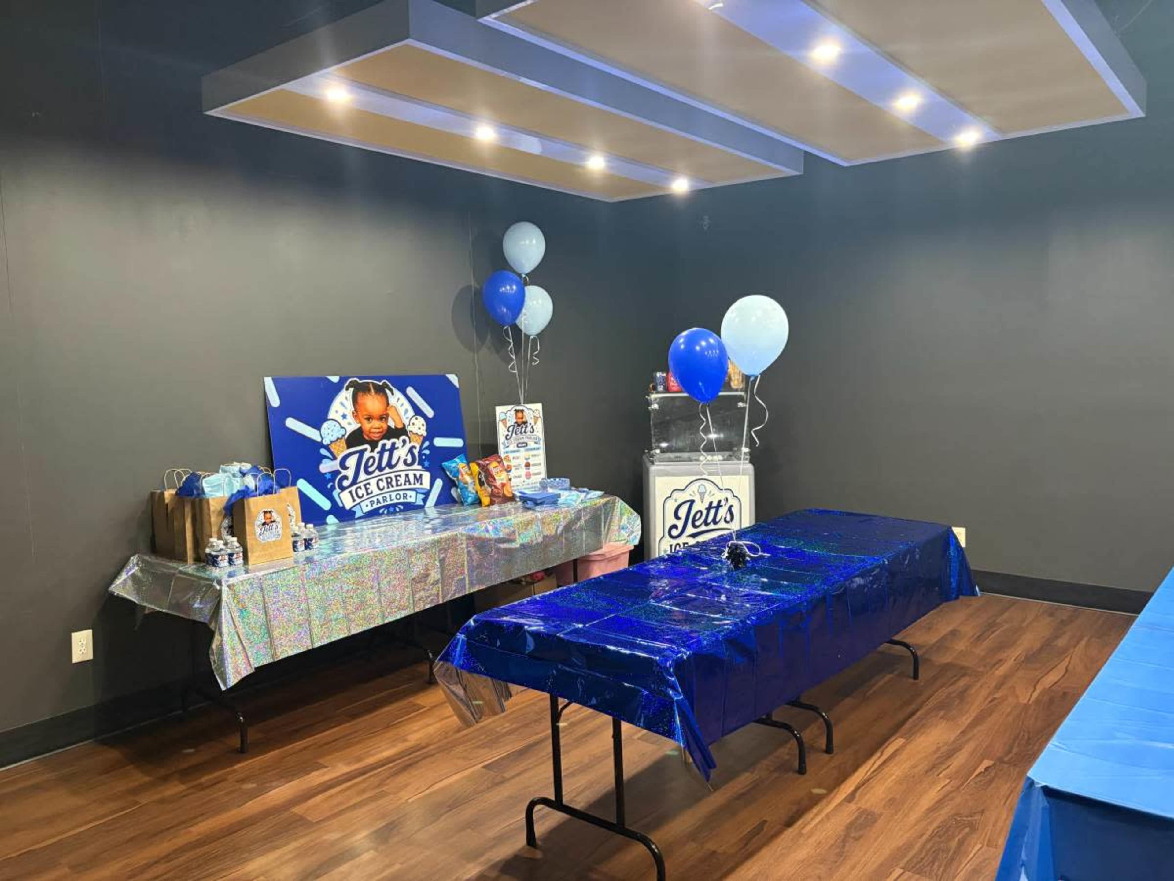 The image shows a party setup with decorated tables featuring ice cream-related displays, balloons, and a sign for "Jett's Ice Cream."