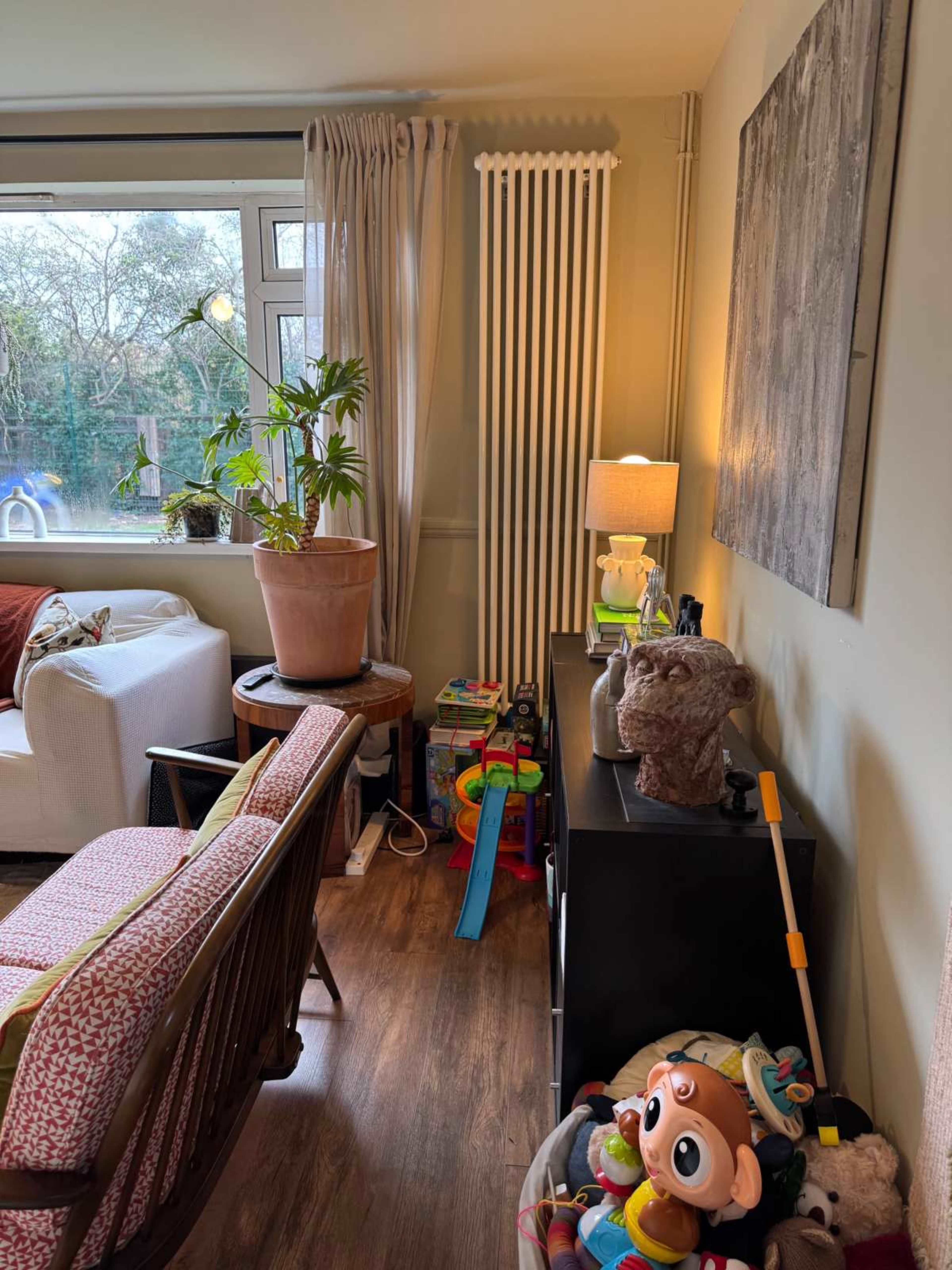 A cozy living room corner features a potted plant, a lamp, a radiator, and various toys on the floor and shelves.