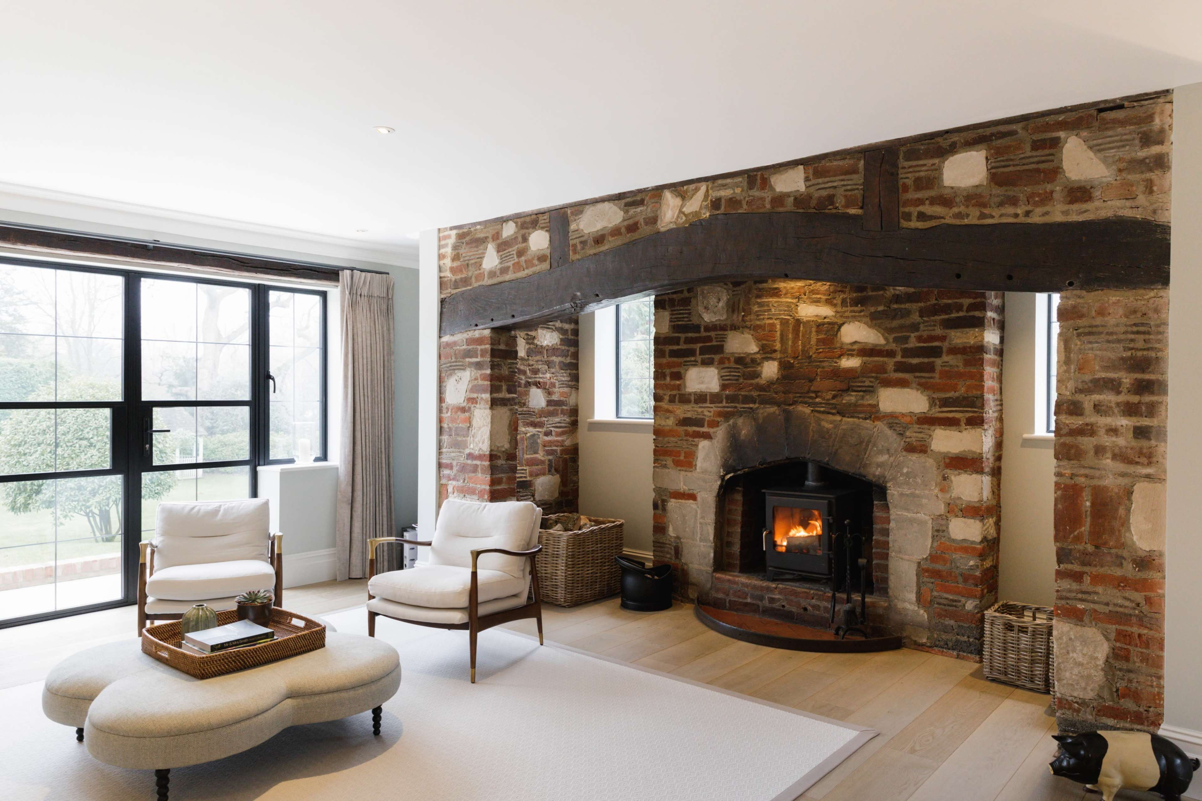 A cozy living room with a stone fireplace as the central feature, flanked by two windows and furnished with modern seating.