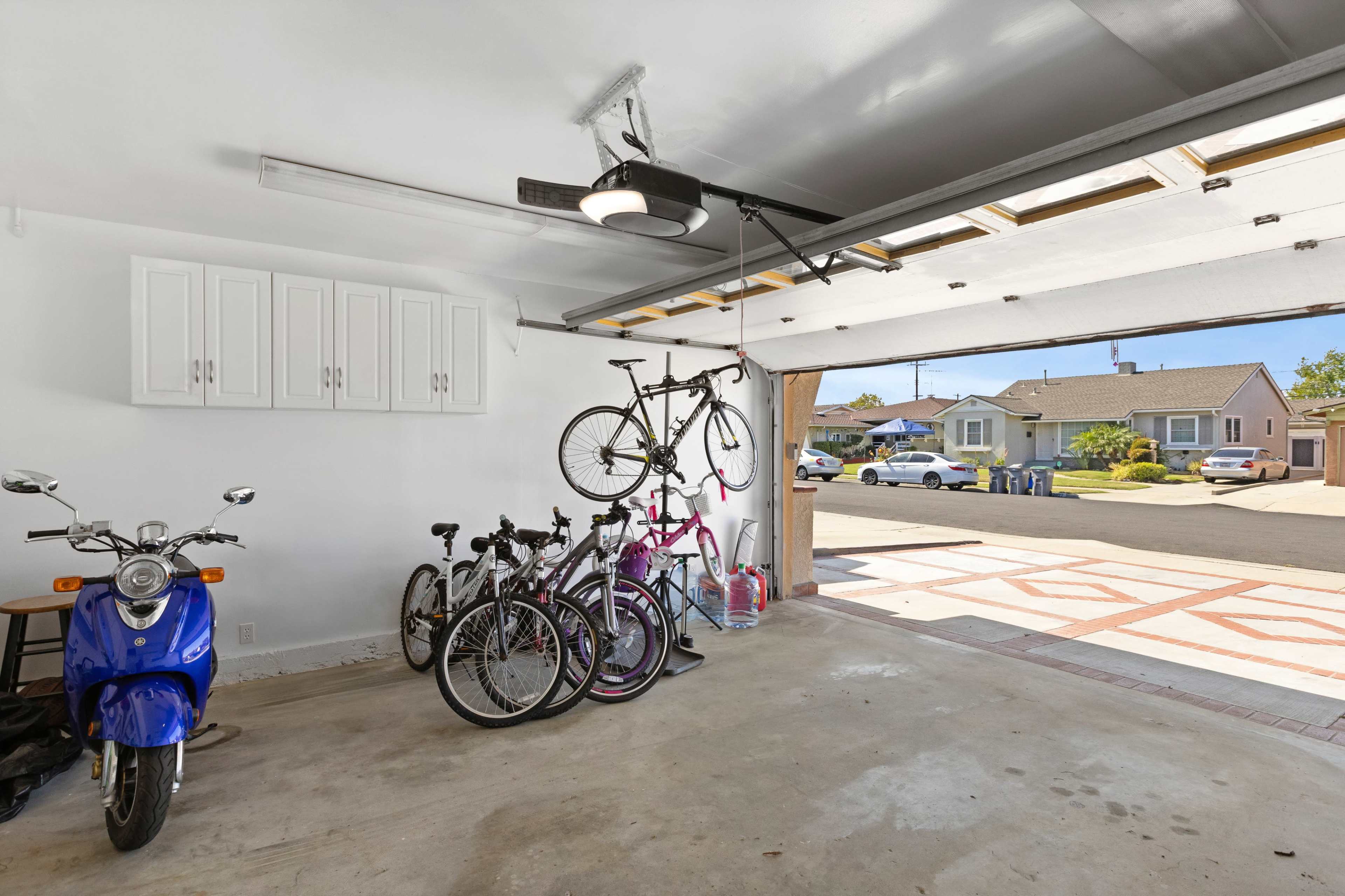 The image shows a two-car garage with several bicycles and a blue scooter parked inside, along with storage cabinets mounted on one wall.