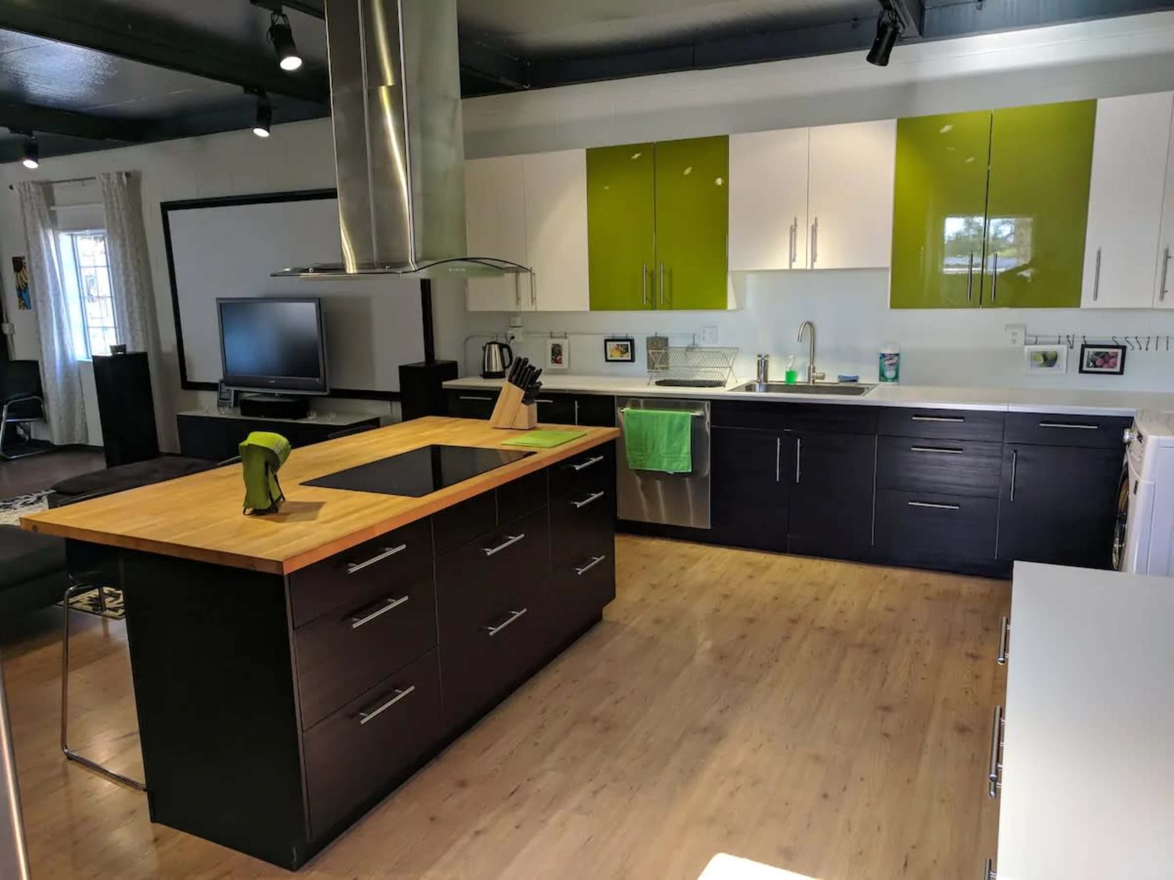 A modern kitchen featuring a central wooden island, dark cabinetry, and green and white upper cabinets with stainless steel appliances.