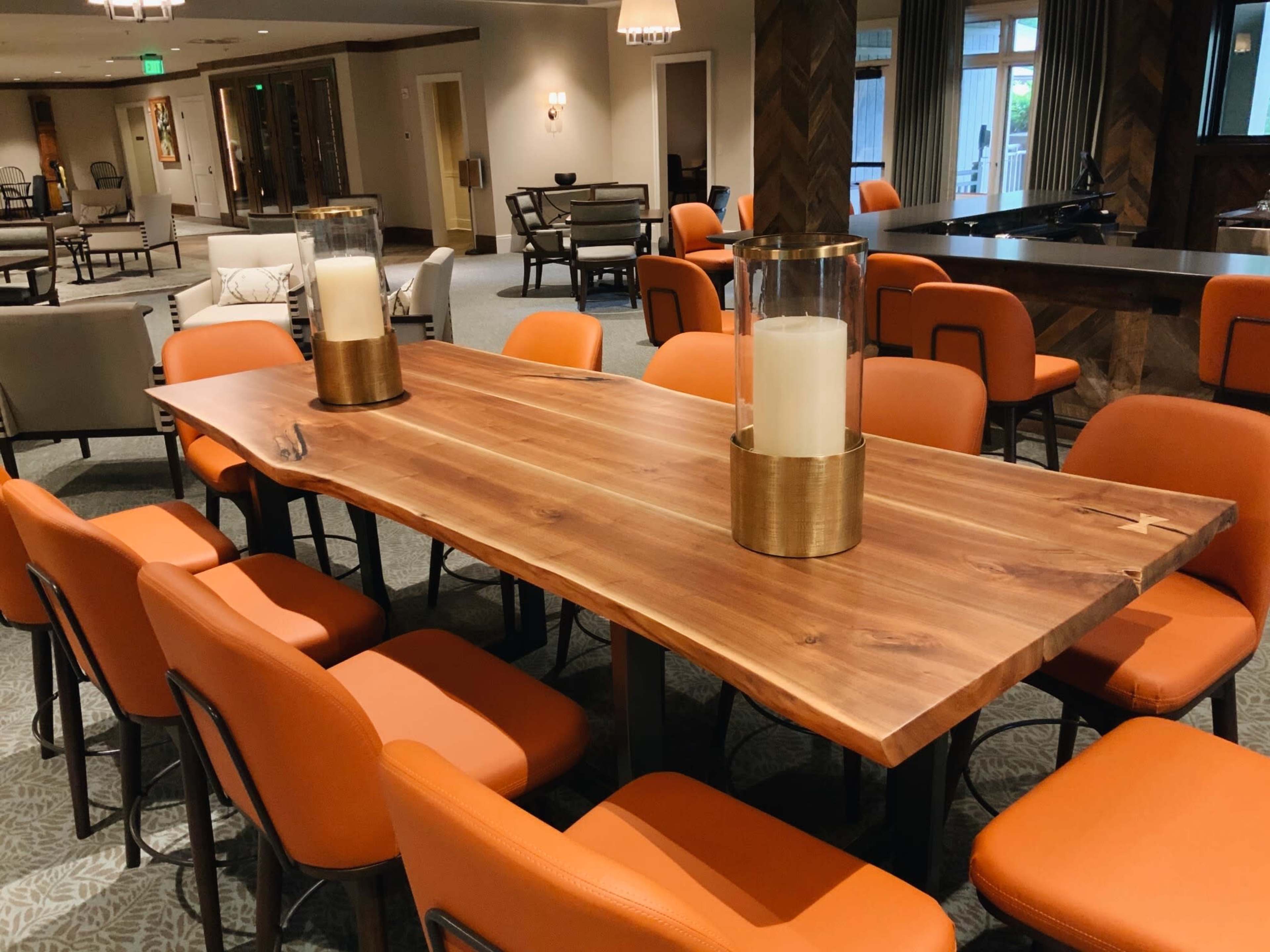 A long wooden dining table with two candle holders is surrounded by orange upholstered chairs in a spacious room.
