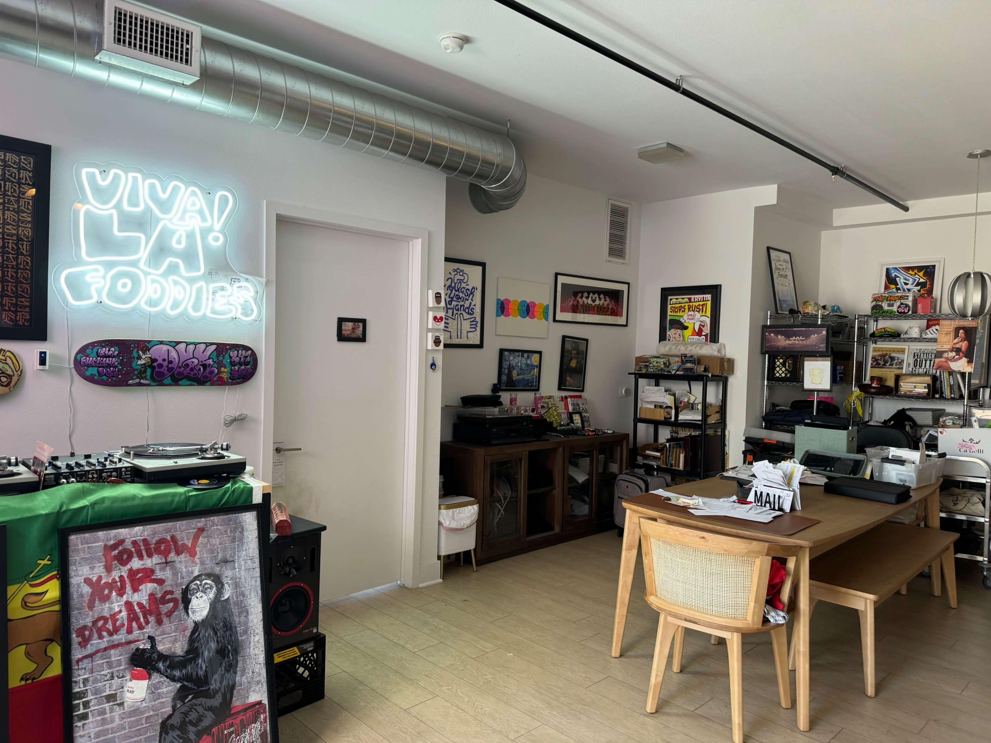 The image shows a room featuring a dining table, shelves filled with various items, a record player, and neon signs on the walls.