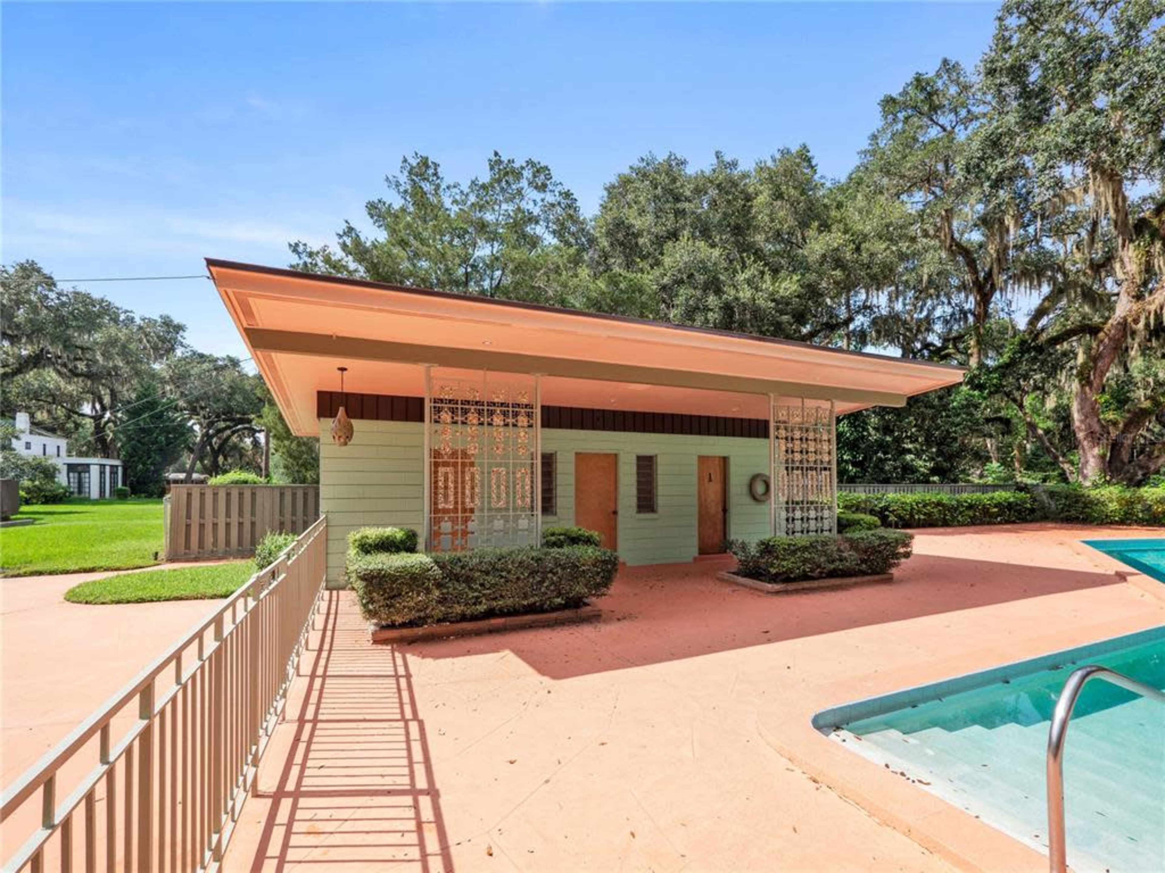 The image showcases a green building with a distinctive roofline, situated next to a swimming pool and surrounded by well-maintained landscaping.