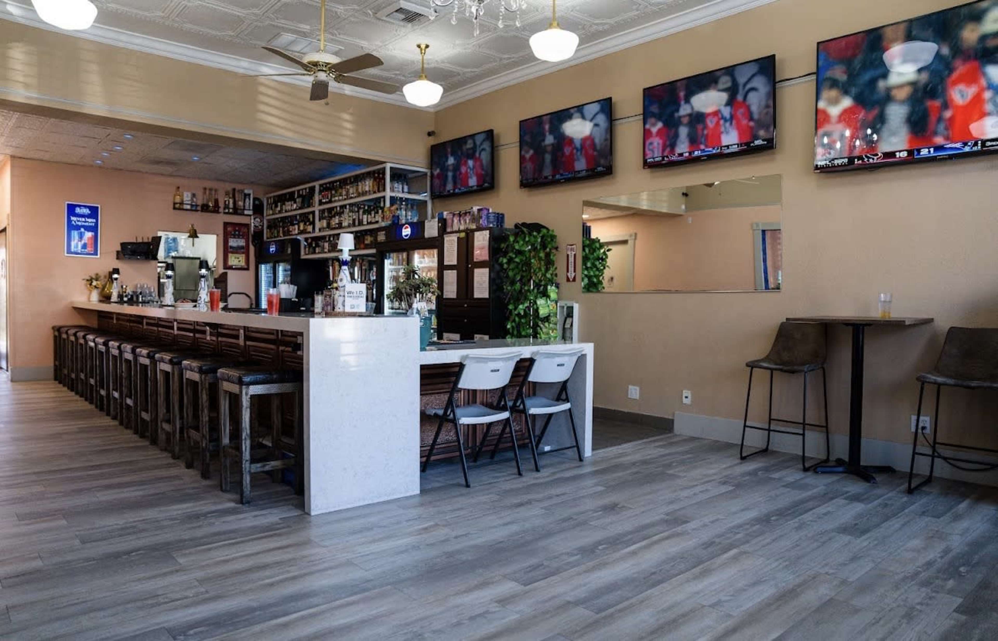 The image shows the interior of a bar or restaurant featuring a long counter, several television screens mounted on the walls, and a mix of seating arrangements.