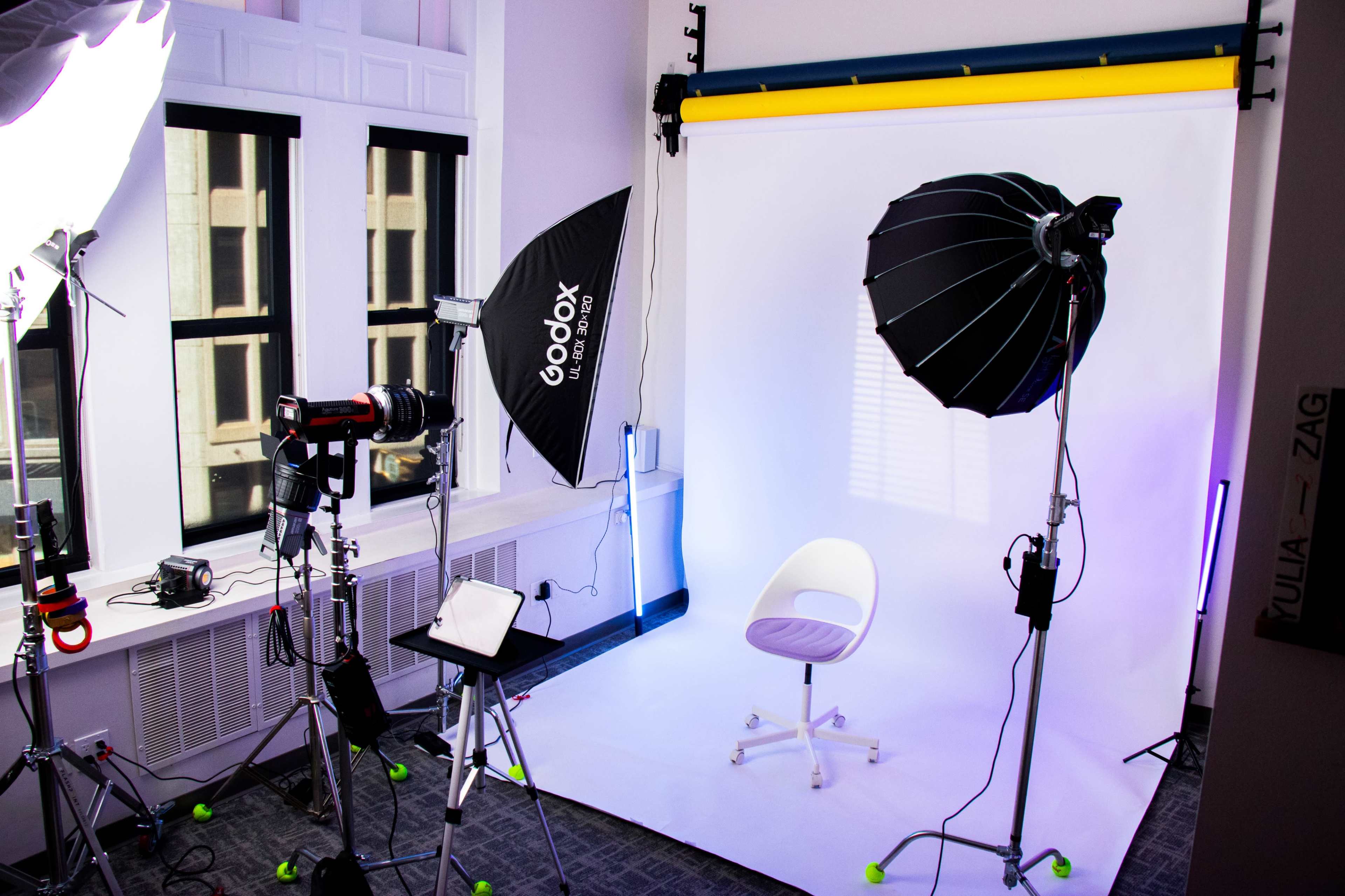 A photography studio is set up with a white backdrop, lighting equipment, and a chair positioned in the center.