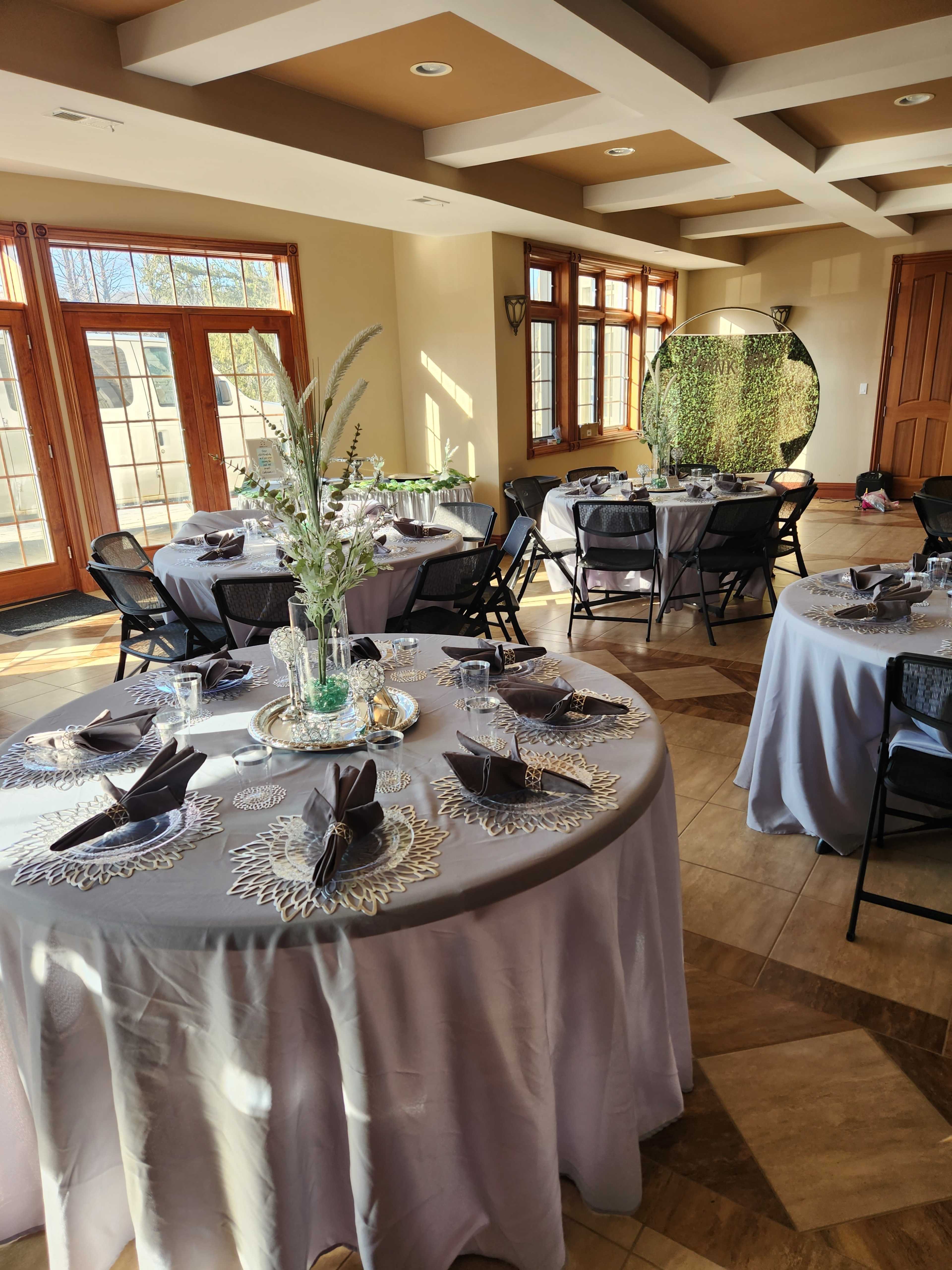 A dining area set with tables covered in gray tablecloths, arranged with floral centerpieces and vintage-style tableware.