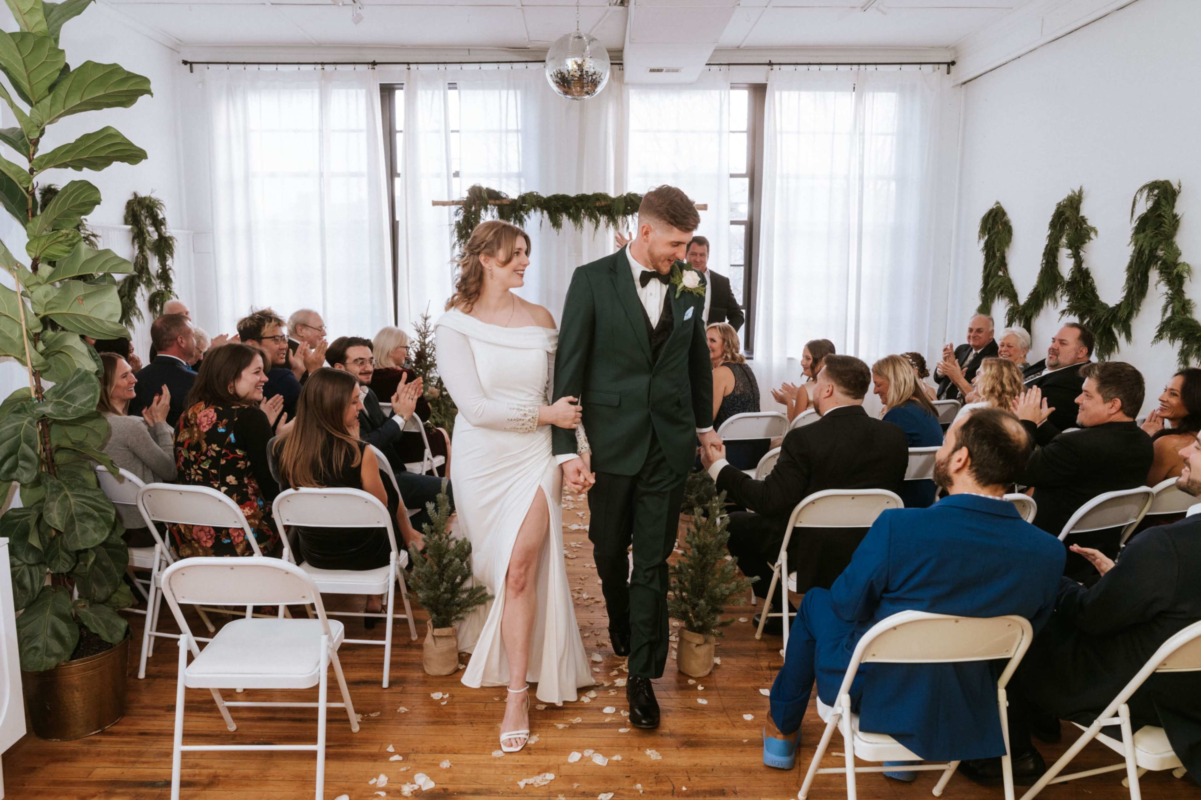 A bride and groom walk hand in hand down the aisle, surrounded by seated guests in a decorated venue.