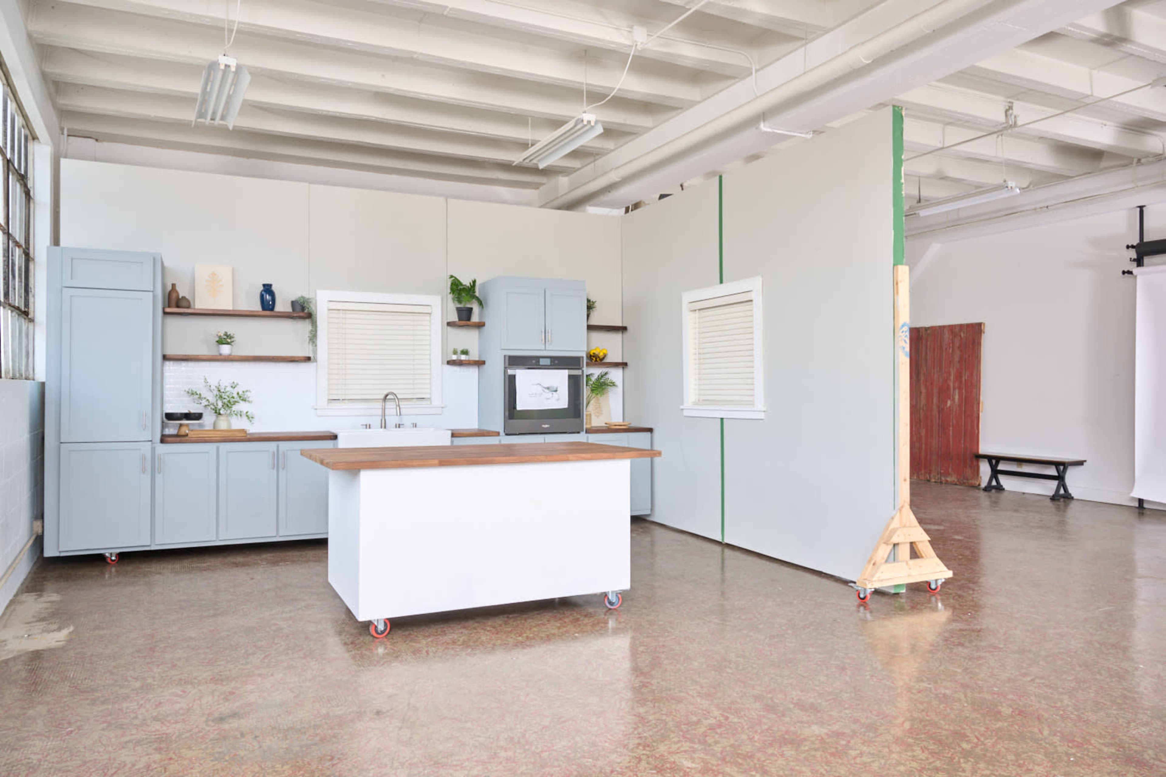 The image shows a modern kitchen space featuring blue cabinetry, a central island with a wooden countertop, and a partitioned area in the background.