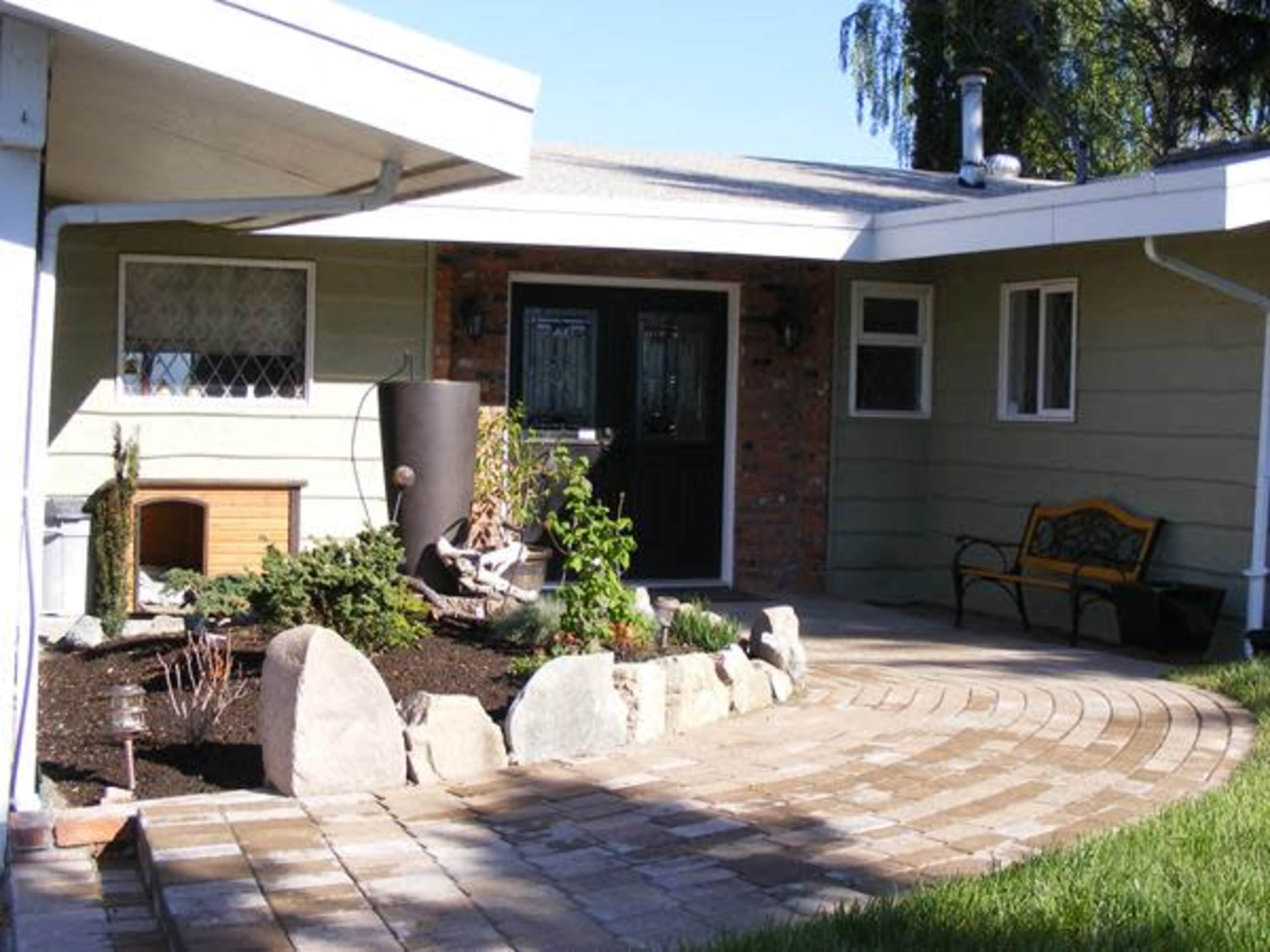 A landscaped patio area with a curved stone pathway leading to a green front door and a garden featuring plants and decorative stones.