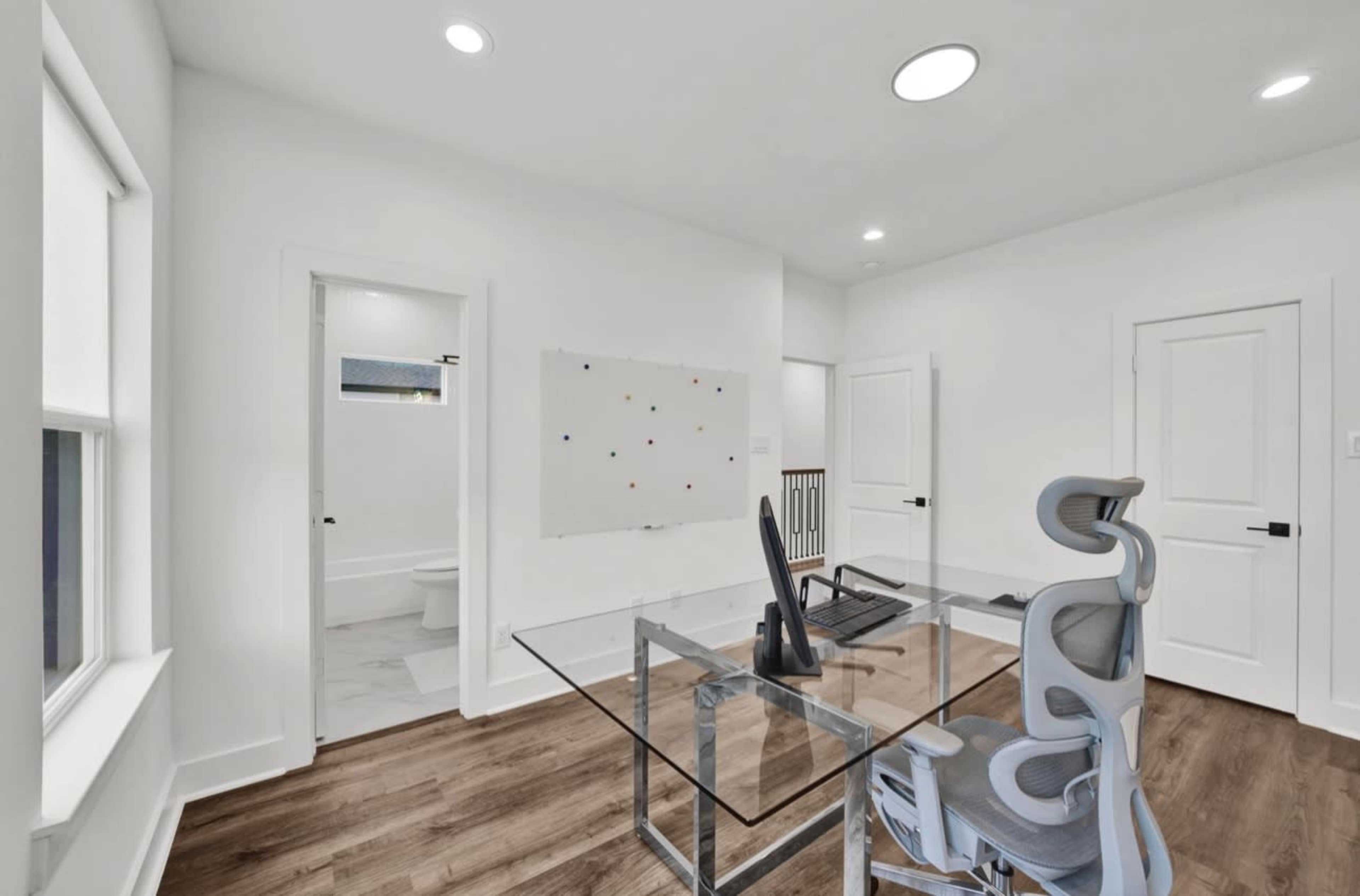 The image shows a modern office space with a glass desk and a swivel chair, featuring a whiteboard on the wall and two doors leading to other rooms.