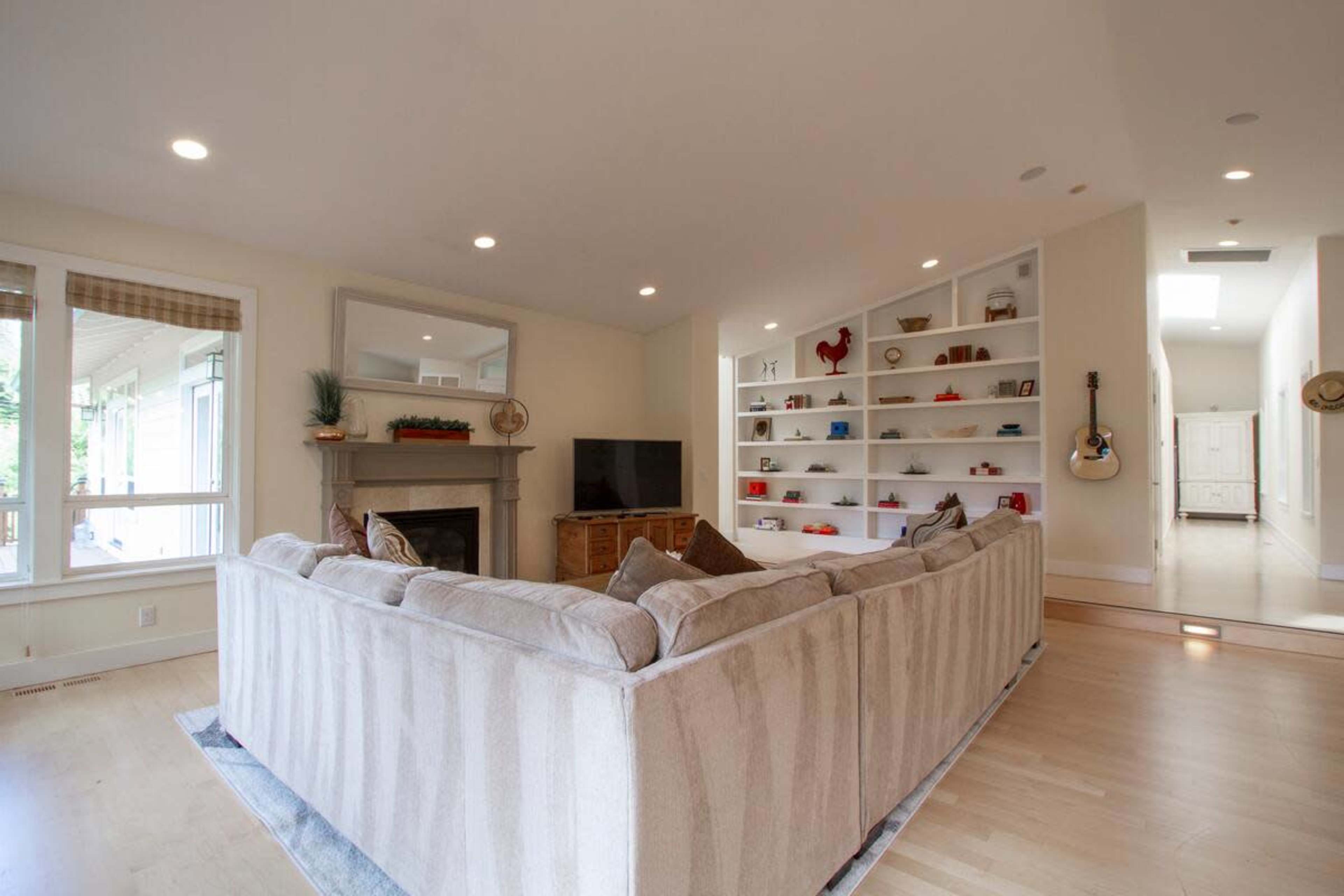 The image shows a spacious living room featuring a large sectional sofa, a fireplace, a mounted television, and built-in shelves displaying various decorative items.