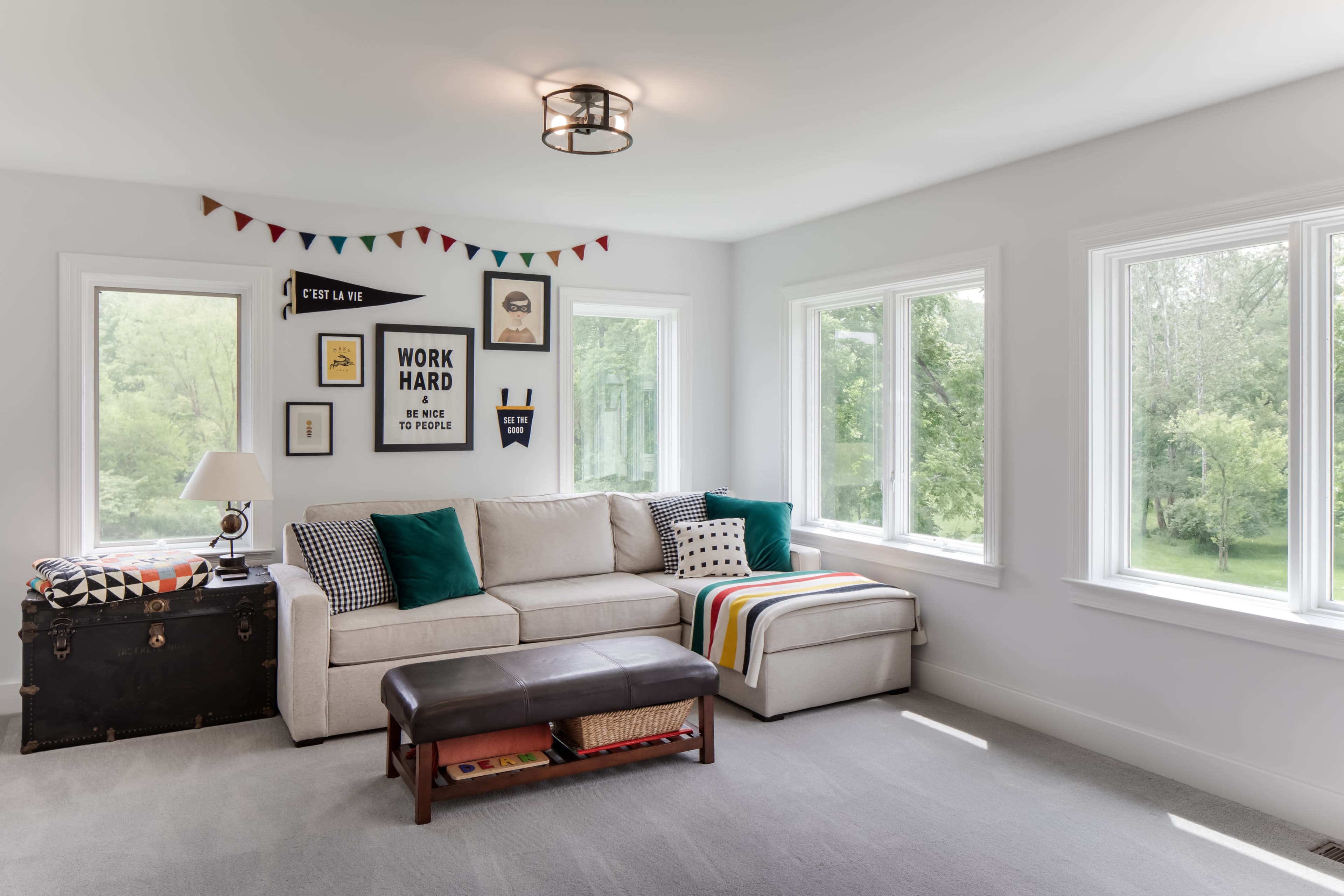A bright and airy living room featuring a beige sectional sofa, a brown coffee table, and large windows overlooking a green landscape.