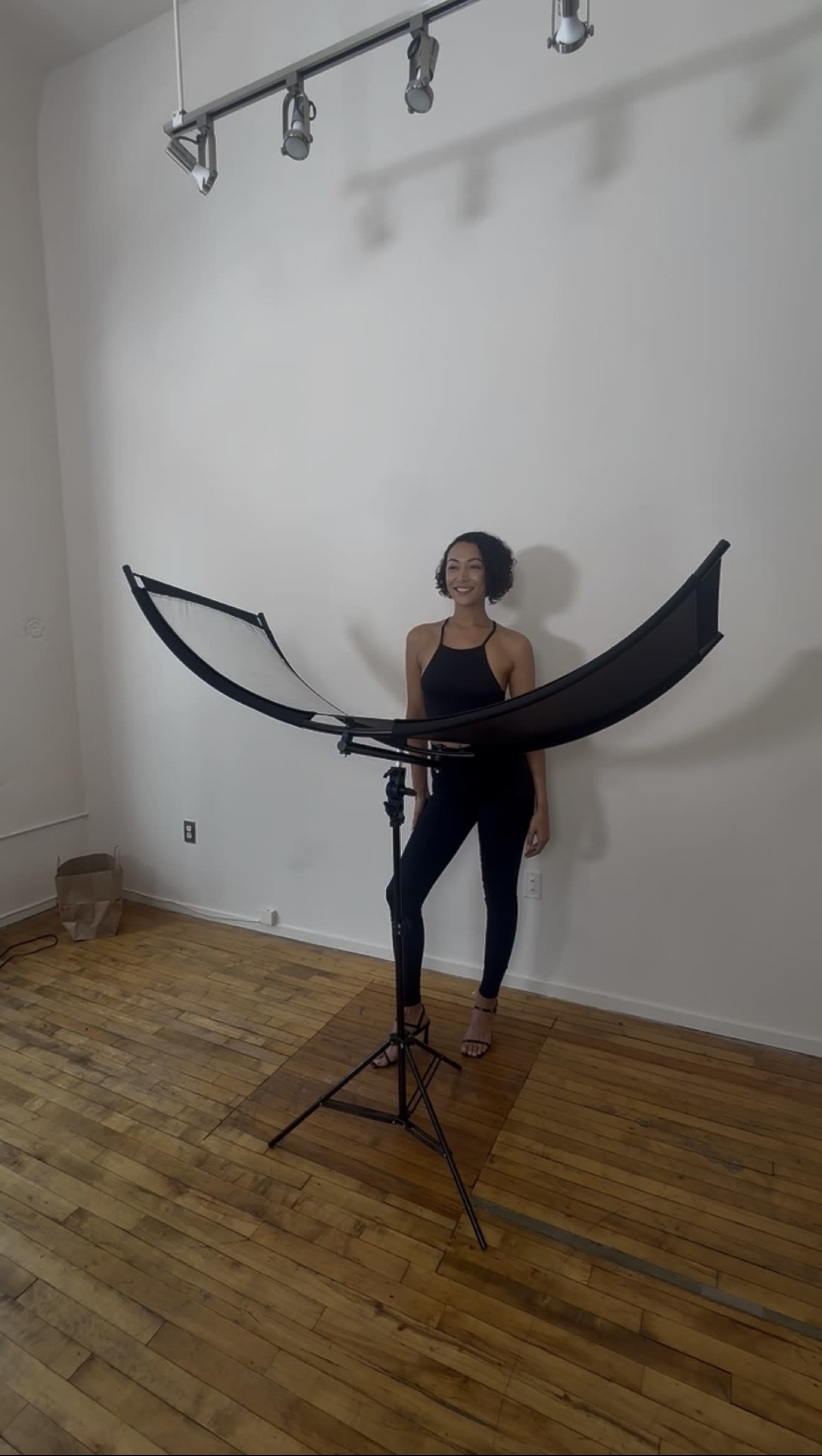 A woman stands in front of a photography backdrop setup in a room with wooden floors.