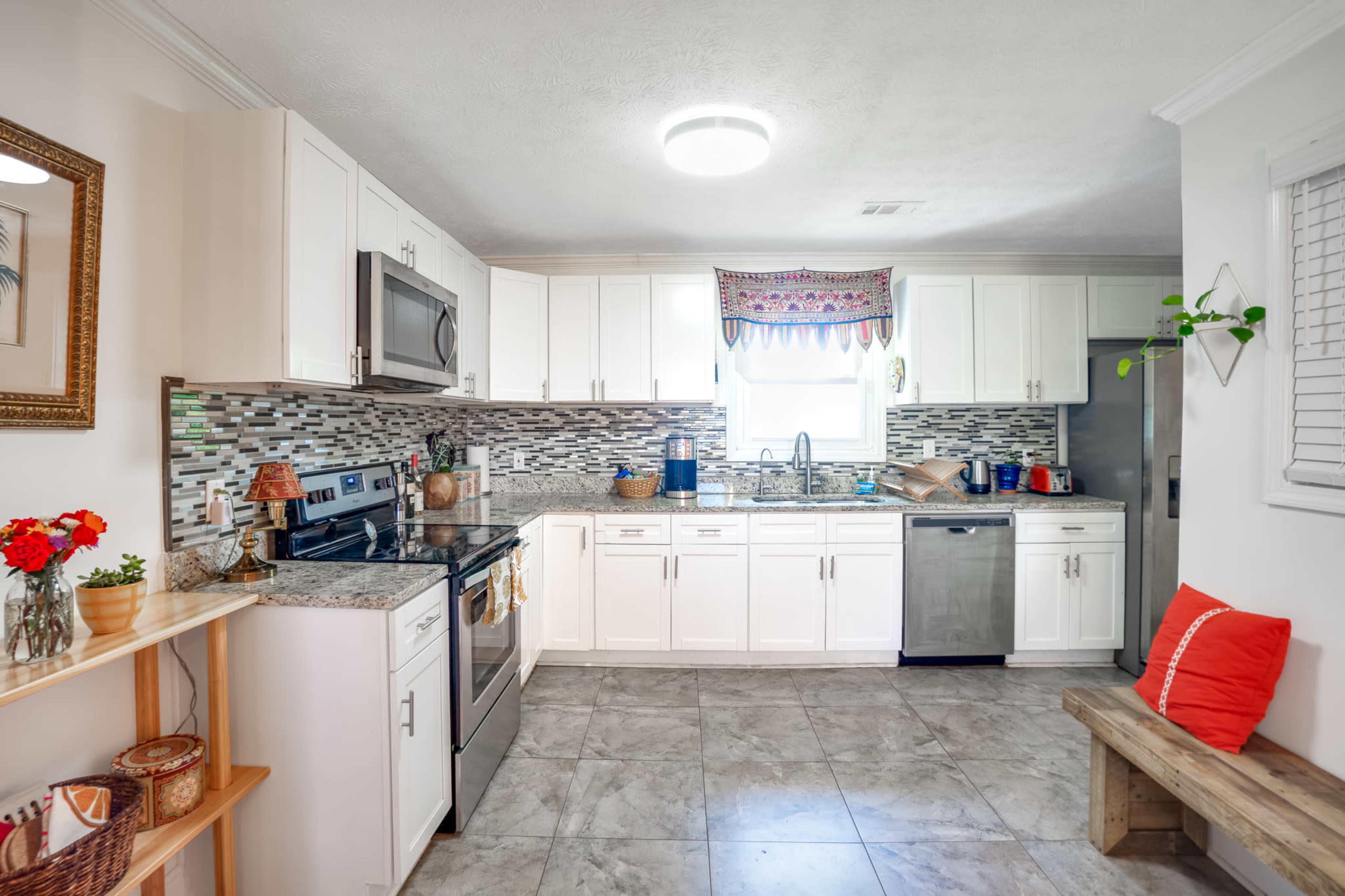 A modern kitchen features white cabinets, stainless steel appliances, and a tiled backsplash with a breakfast nook on the side.