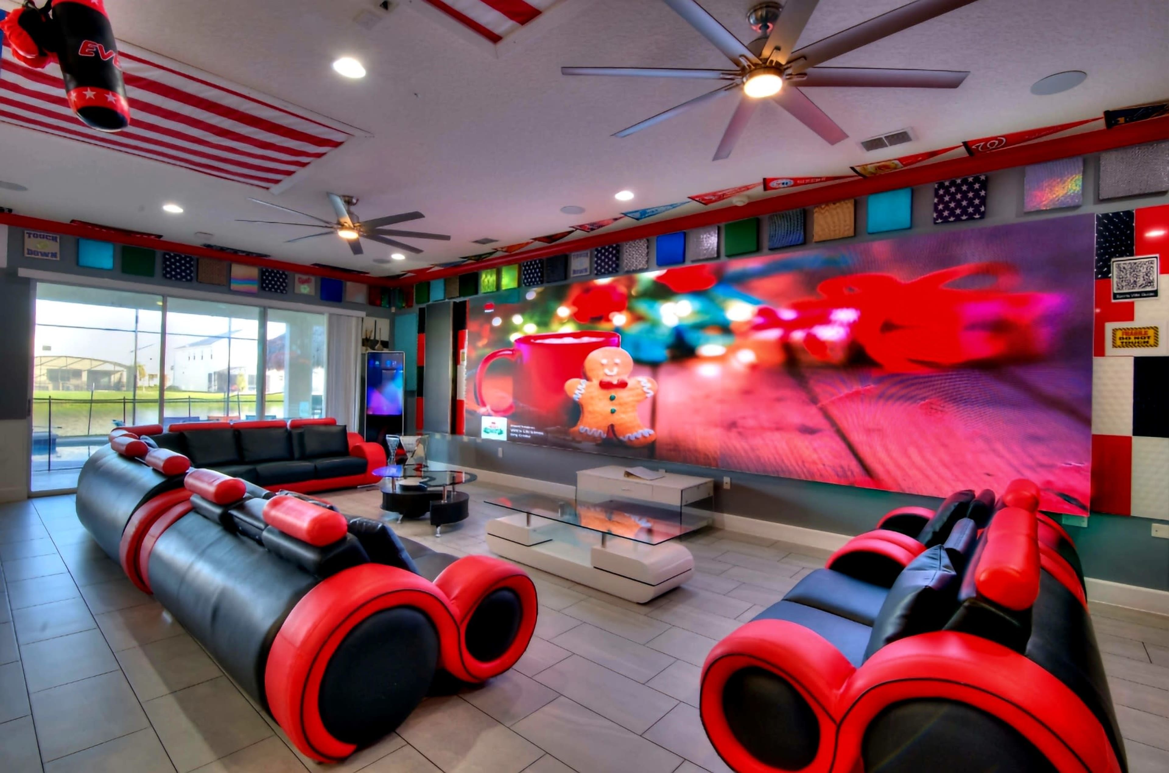 The room features a modern lounge area with red and black furniture, a large screen displaying colorful decor, and an extensive wall adorned with various flags.