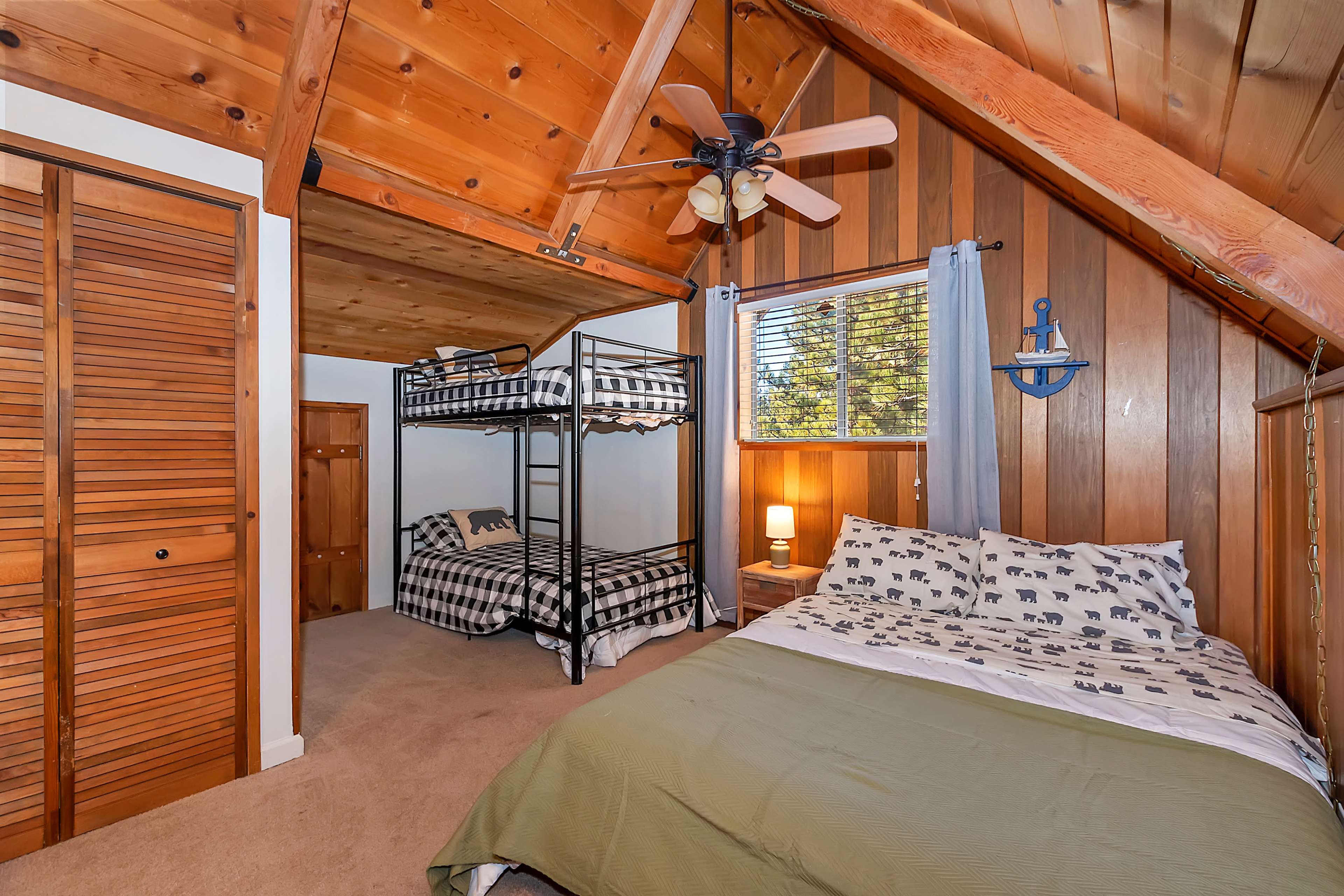 A cozy bedroom with wood-paneled walls, featuring a bunk bed, a double bed, and a ceiling fan.