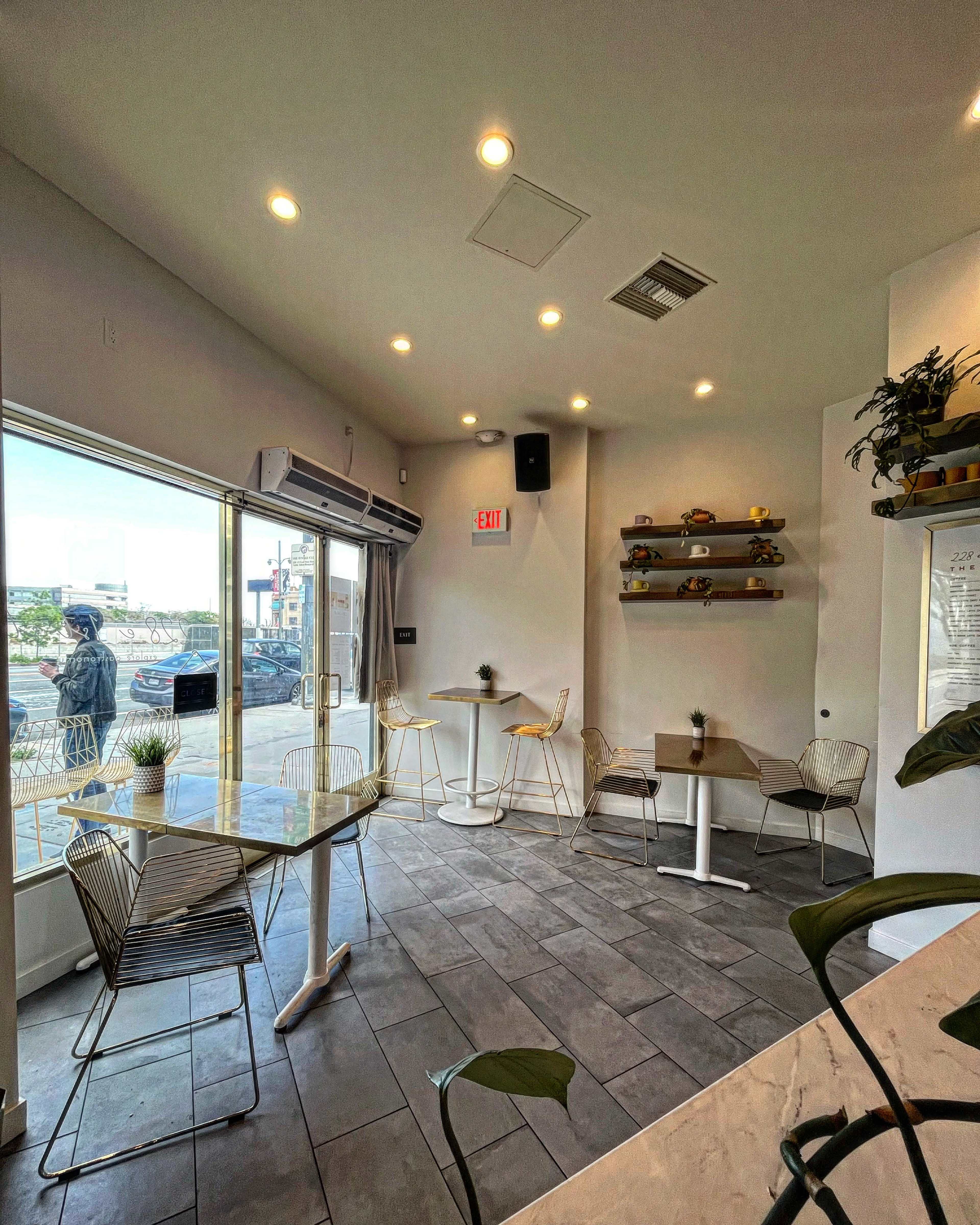 A modern café interior with a glass table, metal chairs, and shelves displaying decorative items, illuminated by recessed lighting.