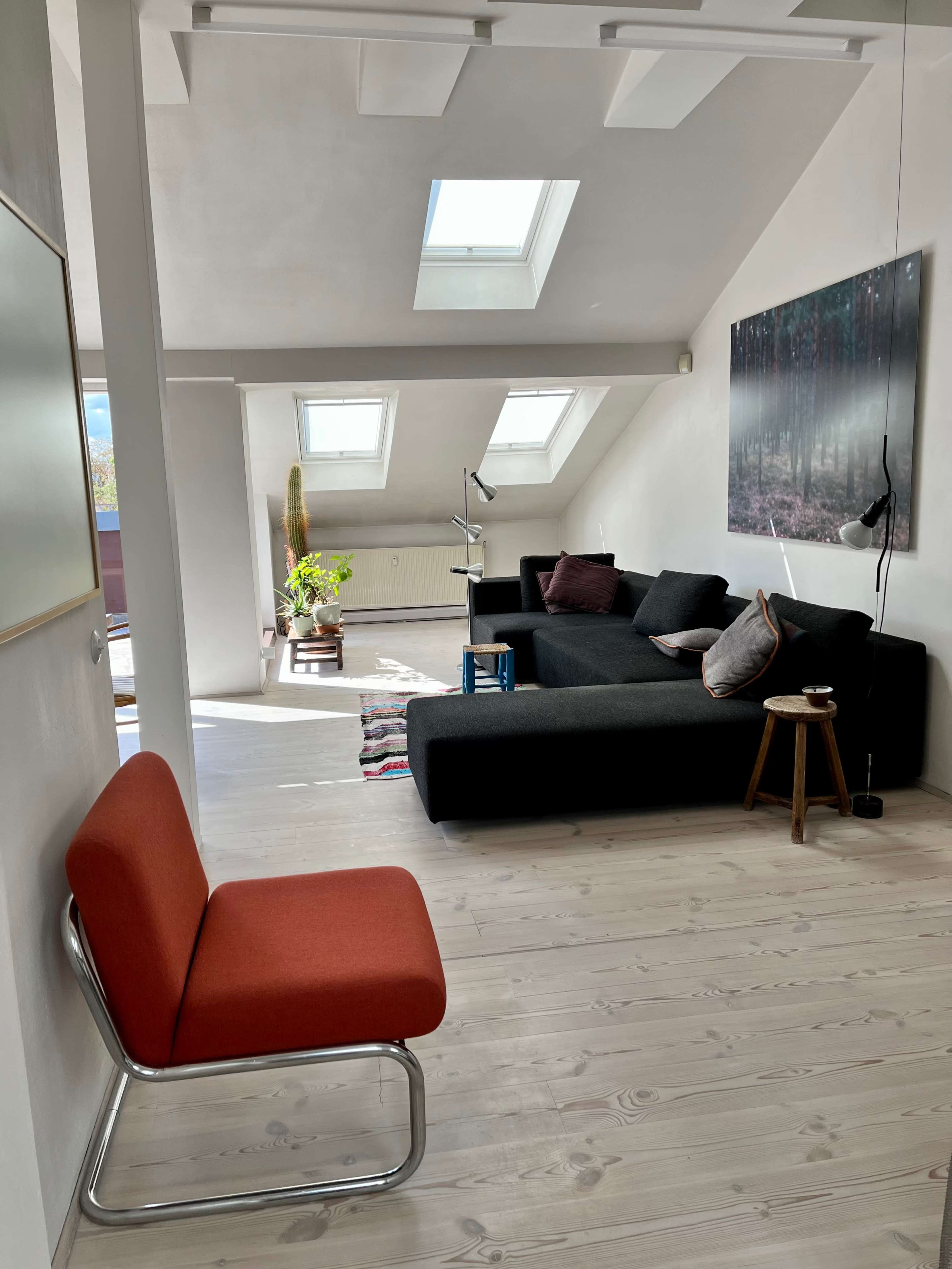 A modern, airy living room with a black sectional sofa, a wooden floor, and skylights illuminating the space.