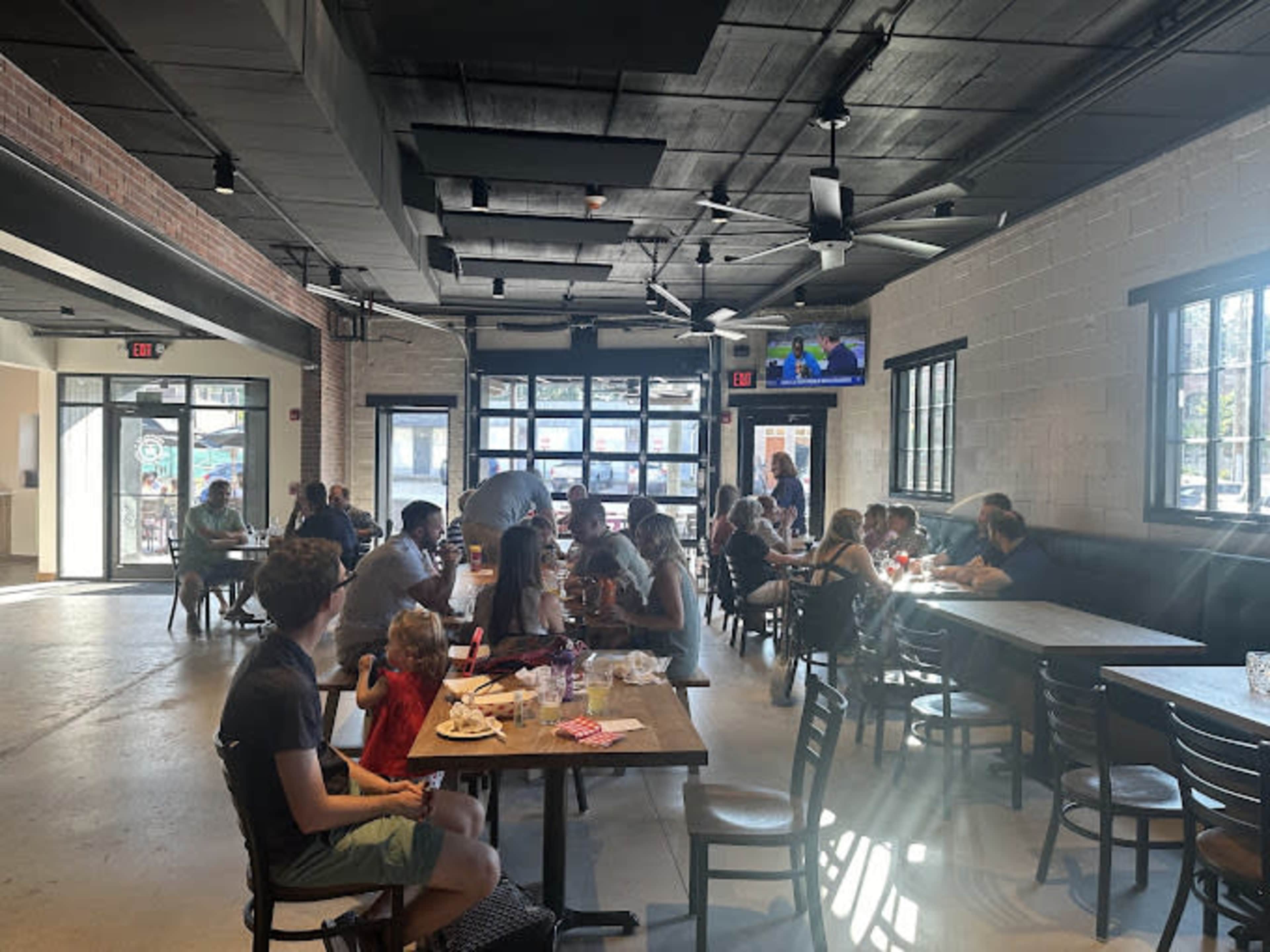The image shows a busy restaurant interior with diners seated at tables, some interacting, while a television is visible in the corner.