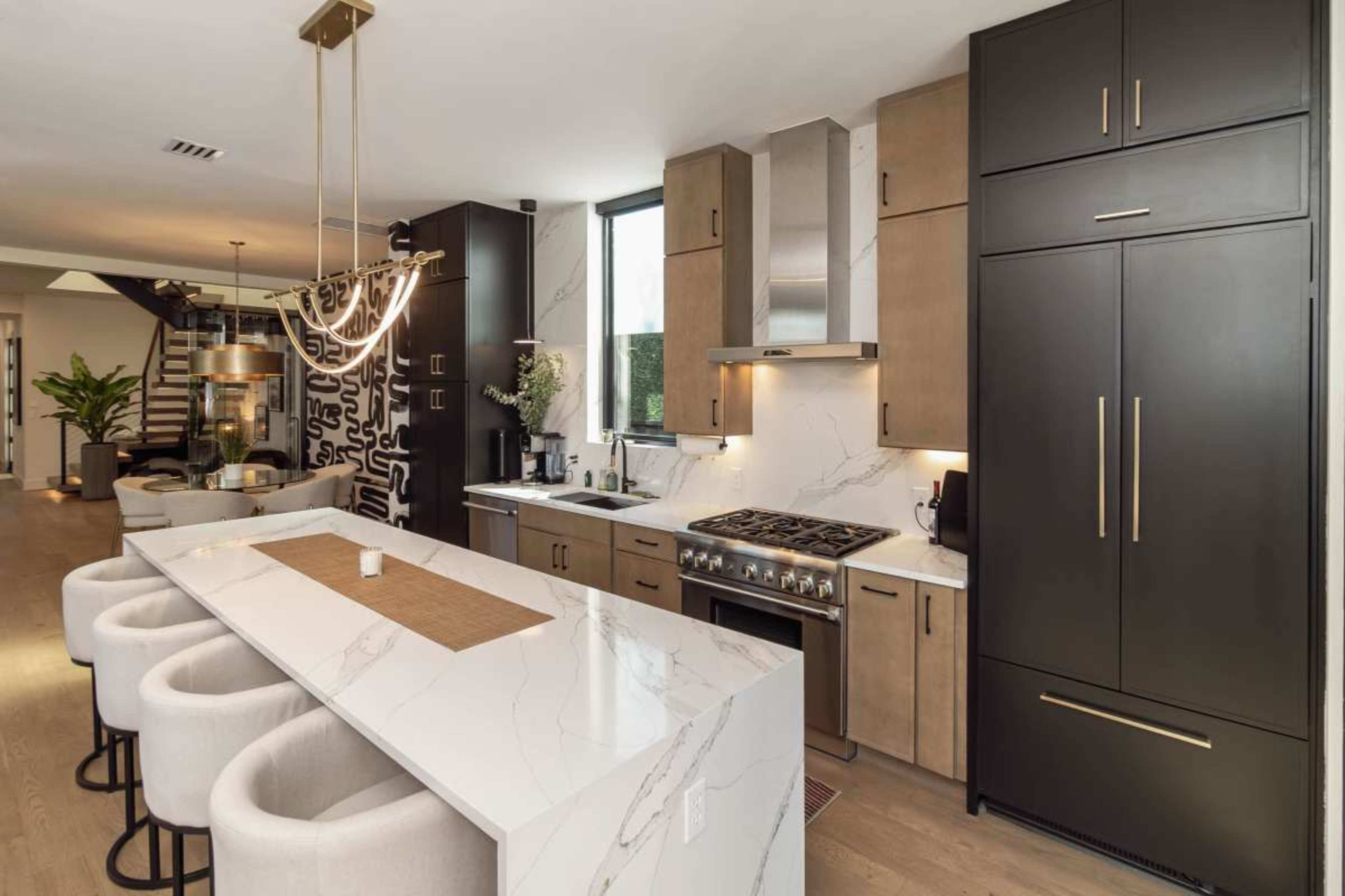 The image shows a modern kitchen featuring a large island with bar seating, sleek cabinetry, and high-end appliances.