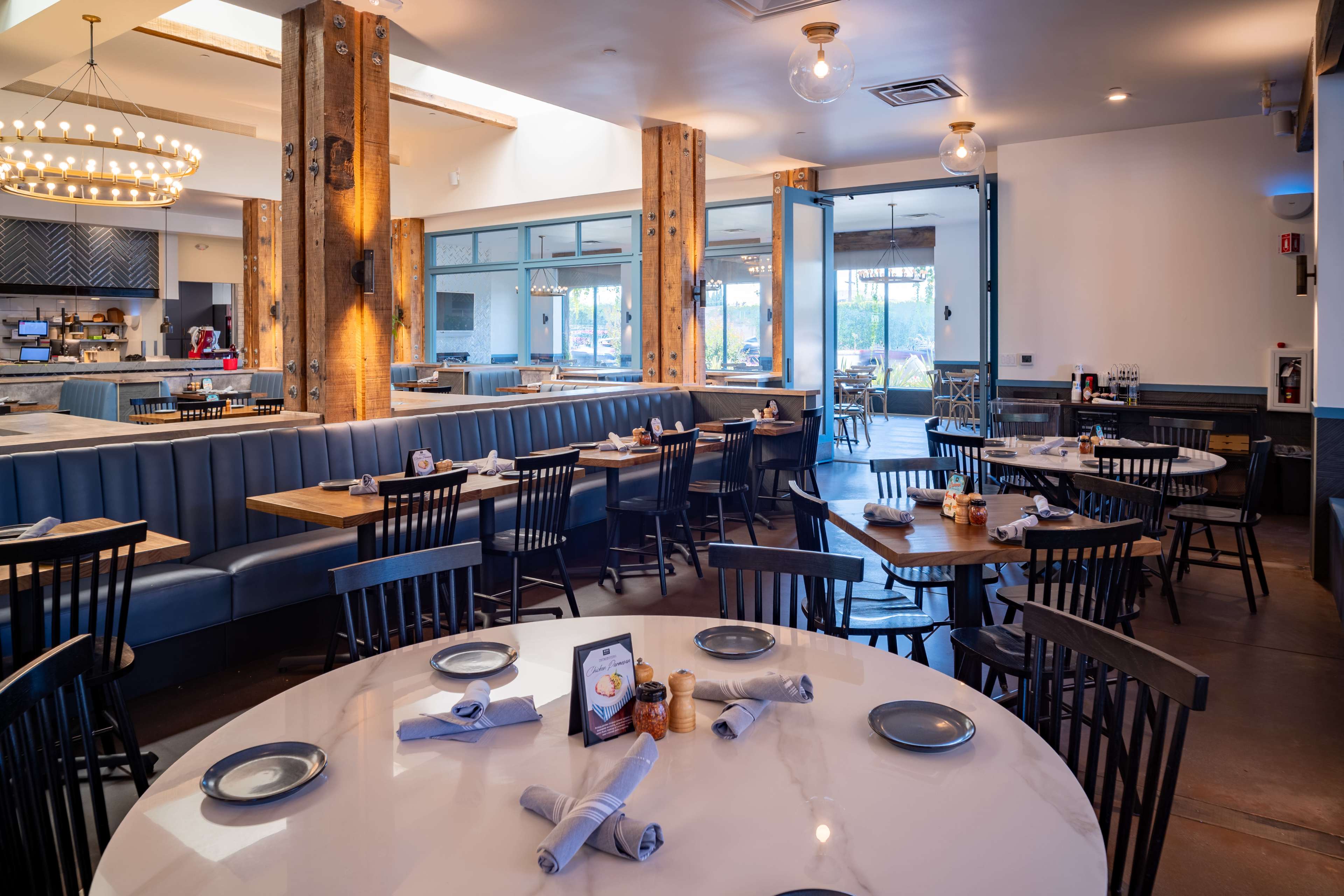 The image shows a spacious restaurant interior with wooden beams, blue upholstered seating, and several tables set with plates and napkins.
