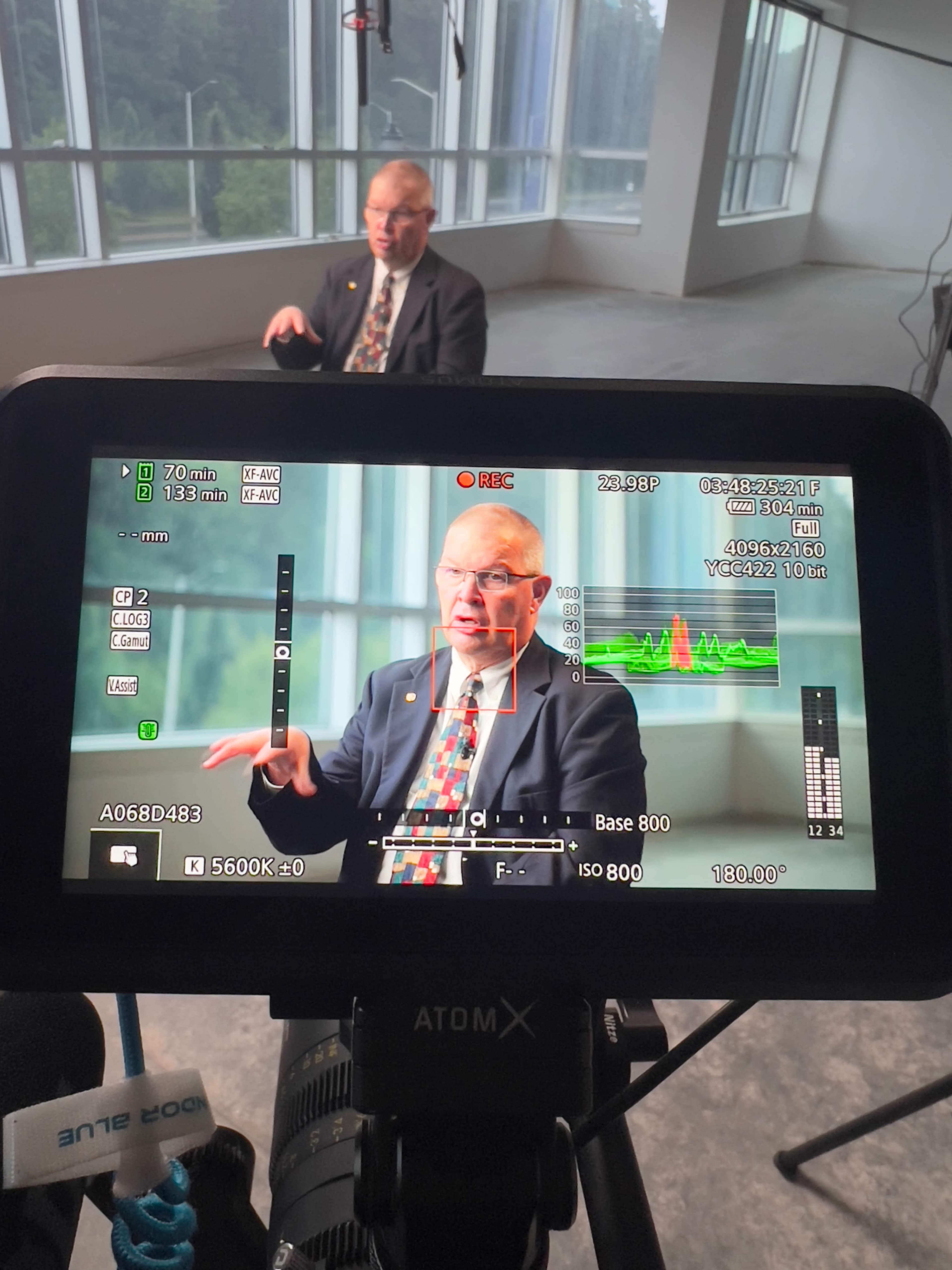 A camera preview displays a man in a suit speaking in front of a large window in a well-lit room.